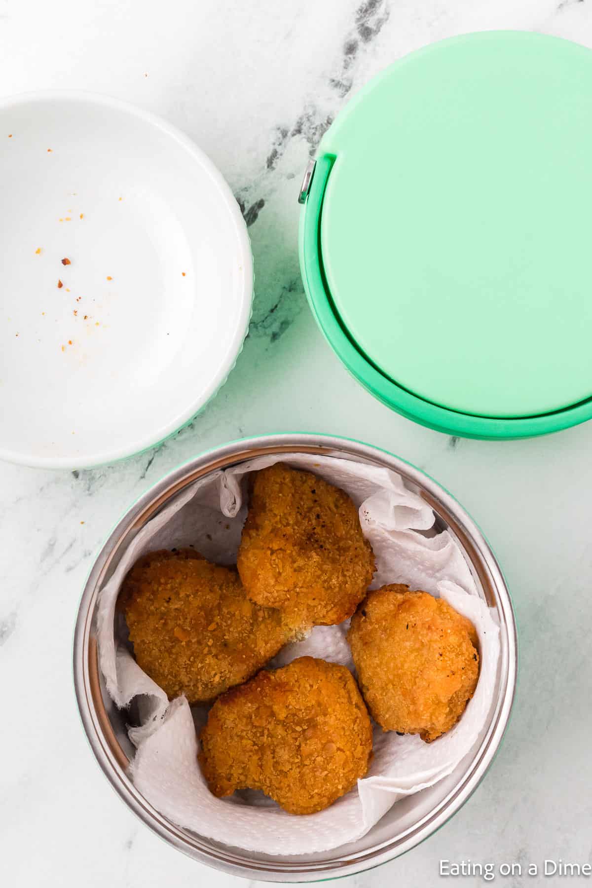 Cooked chicken nuggets in the insulated container with a paper towel and bowl on the side