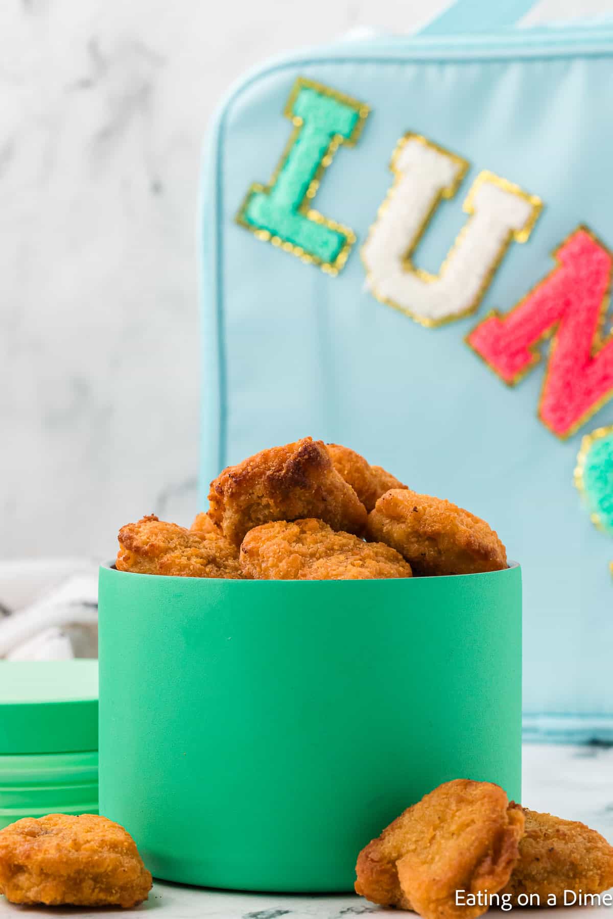 Chicken Nuggets in a blue lunch container with chicken nuggets on the side with a lunch box in the background