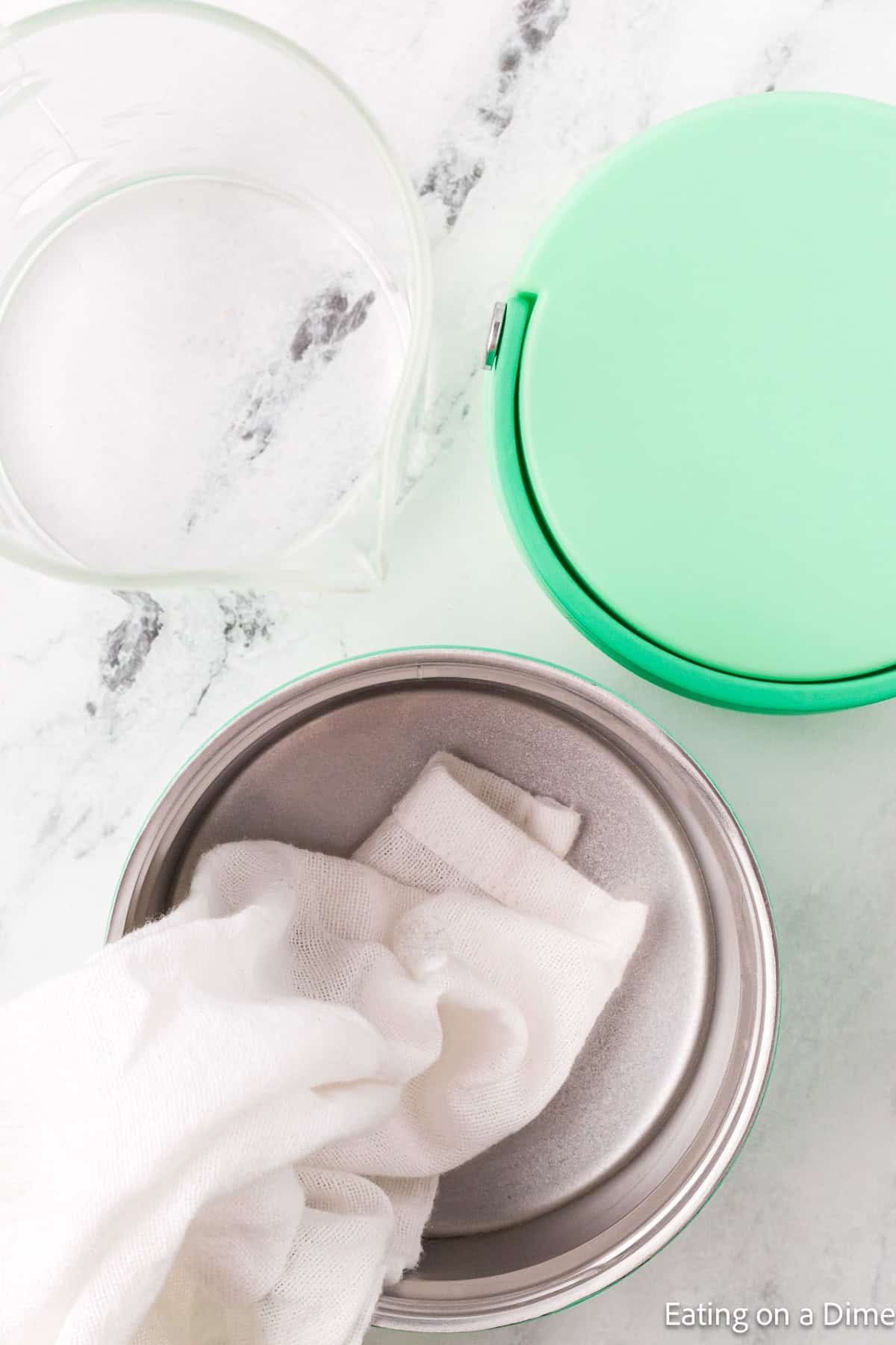 Towel draped in insulated container with a lid and a bowl of water on the side