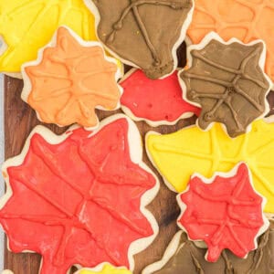 A collection of Fall Leaf Sugar Cookies decorated with colorful icing in autumn hues of red, yellow, orange, and brown, arranged on a wooden surface. The cookies capture the essence of fall with their vibrant seasonal colors and intricate leaf designs.