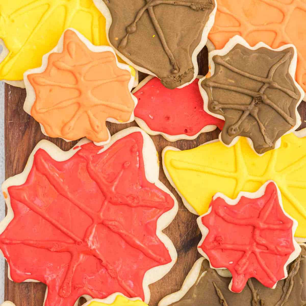 A collection of Fall Leaf Sugar Cookies decorated with colorful icing in autumn hues of red, yellow, orange, and brown, arranged on a wooden surface. The cookies capture the essence of fall with their vibrant seasonal colors and intricate leaf designs.