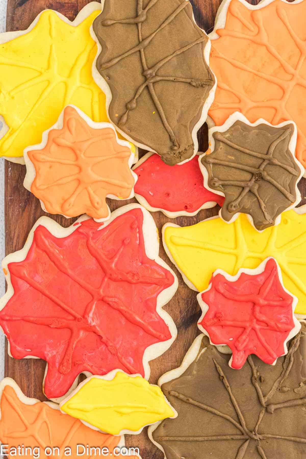 A collection of Fall Leaf Sugar Cookies with colorful icing, arranged on a wooden surface. The cookies are decorated with vibrant red, orange, yellow, and brown icing, resembling autumn leaves.