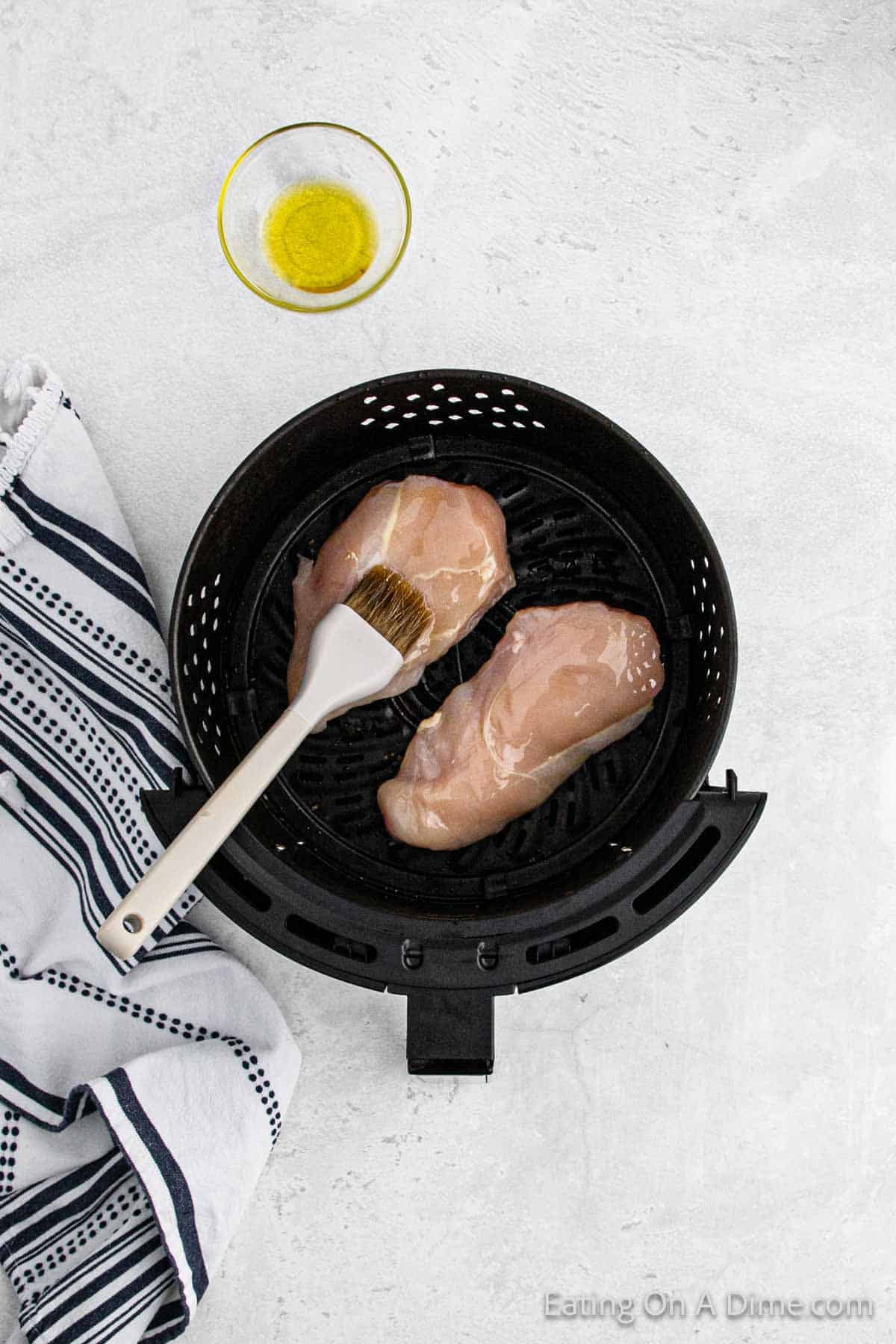 Brushing oil on the chicken breast in the air fryer basket