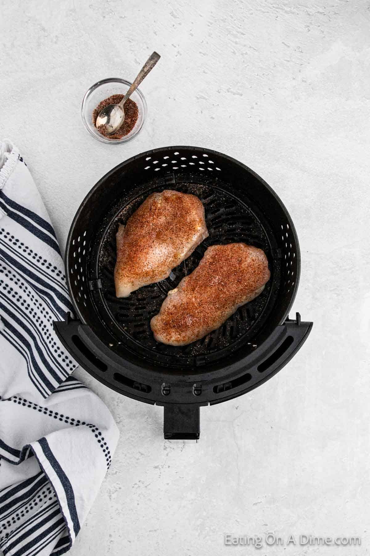Toping the chicken breast in the air fryer basket with the seasoning blend