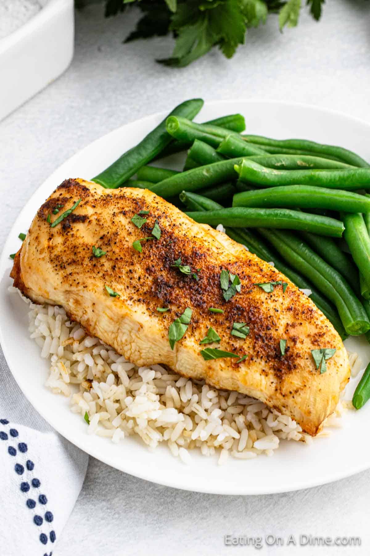 Air Fryer chicken breast on top of white rice on a plate with a side of fresh green beans