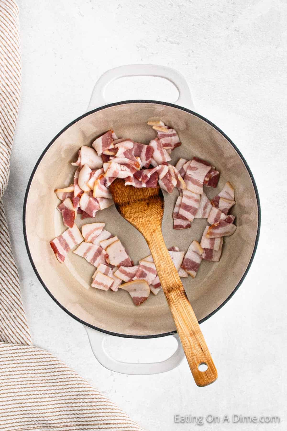 Cooking chopped bacon in a large pot with a wooden spoon