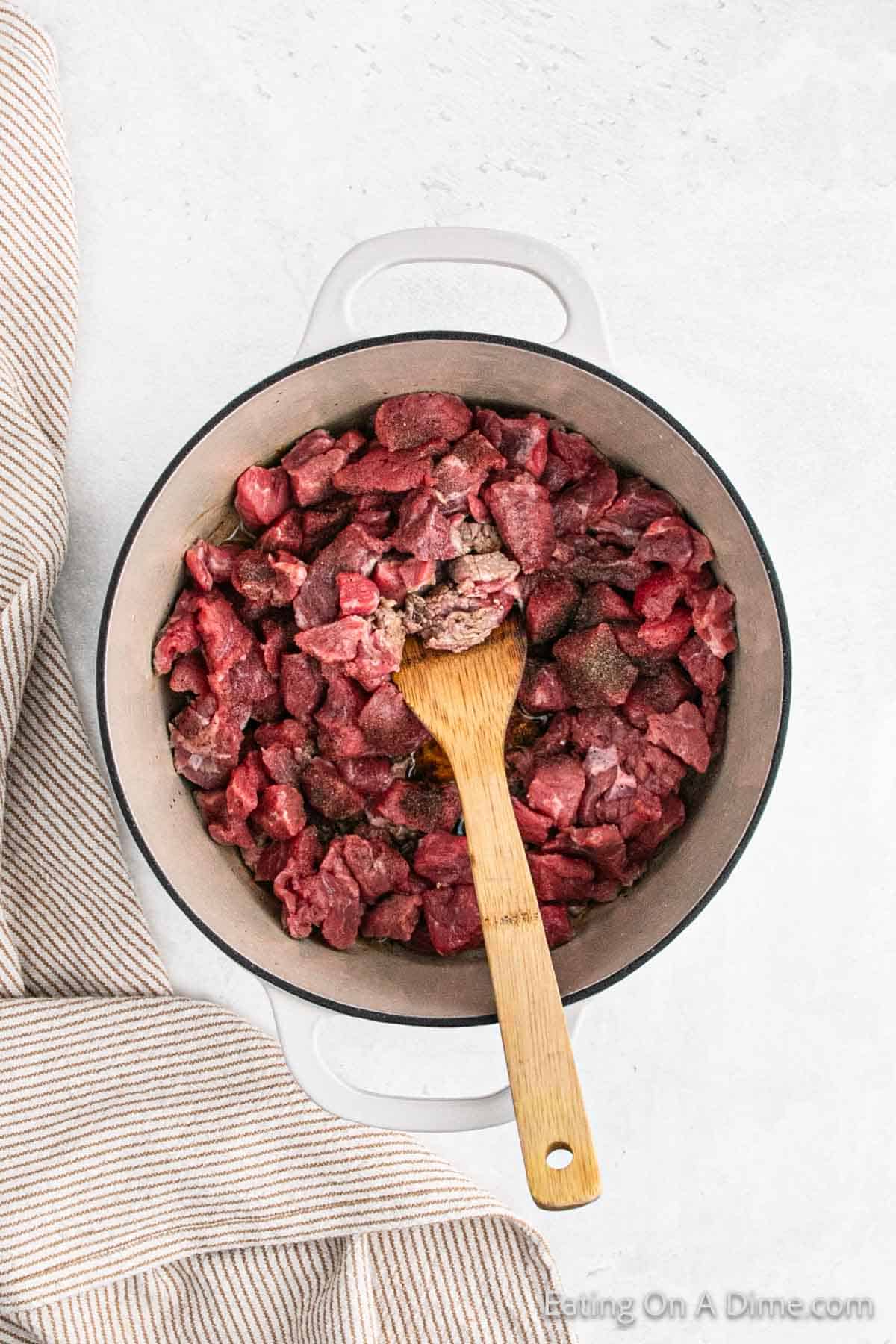 Cooked beef stew in a large pot with a wooden spoon