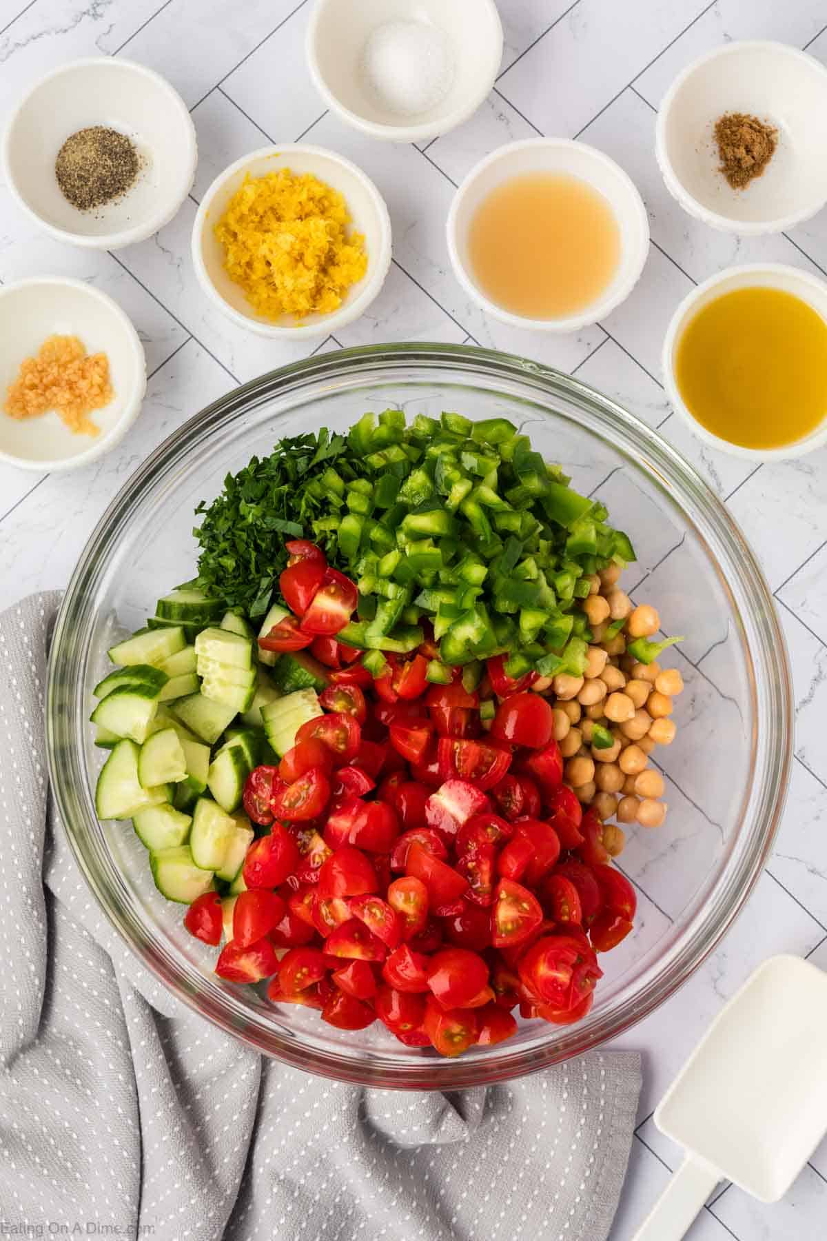 Chopped cherry tomatoes, slice cucumber, bell peppers, chickpea and parsley in a bowl with small bowls of minced garlic, pepper, salt, lemon zest