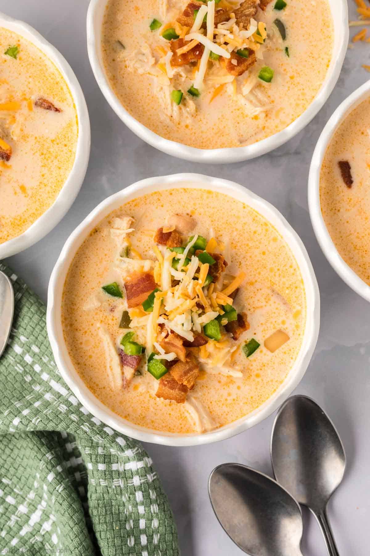 Jalapeno Popper Chicken Soup in white bowls topped with shredded cheese, diced jalapenos and bacon