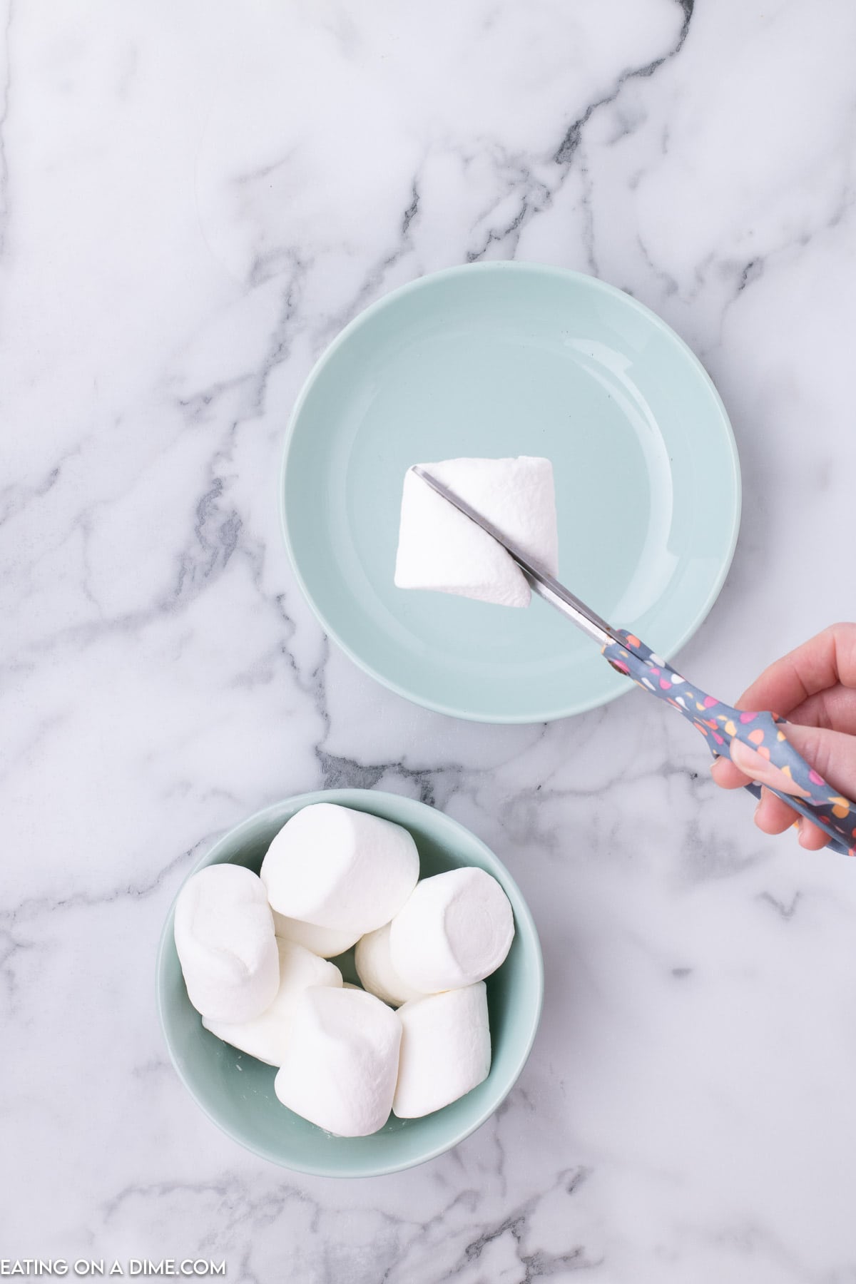 Large marshmallows in a bowl with one being cut with scissors 