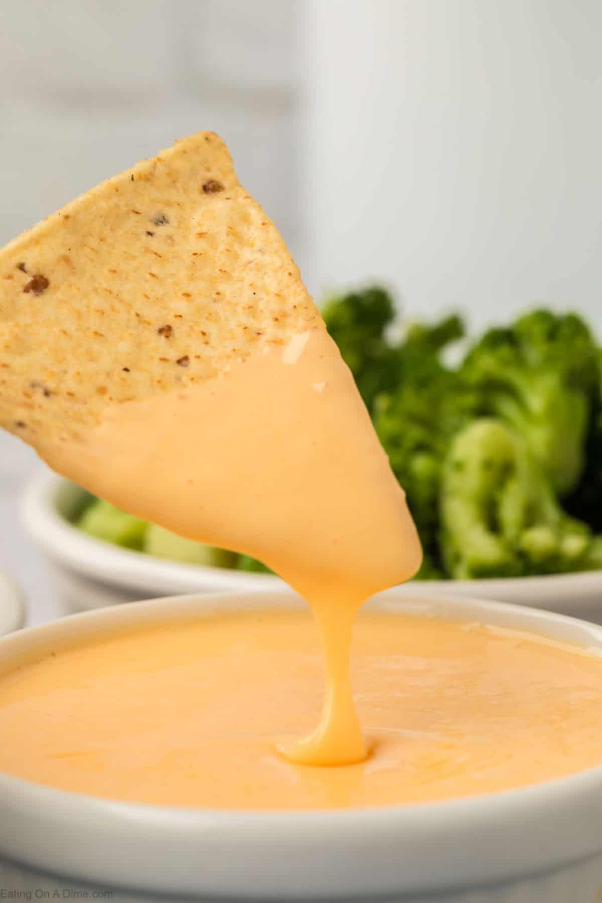 A chip being dipped into homemade American cheese sauce with the sauce dripping off the chip back into the bowl.  