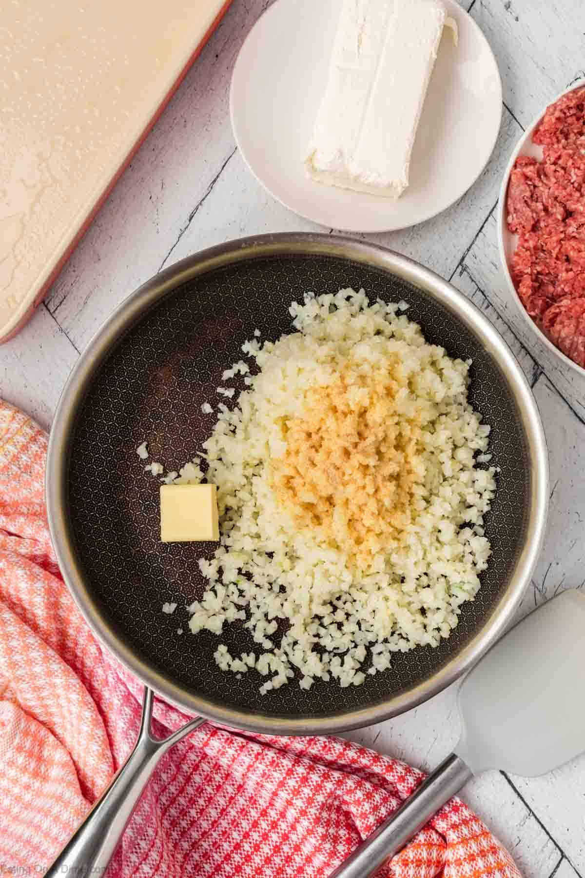 Cauliflower Rice in a skillet topped with seasoning and slice butter