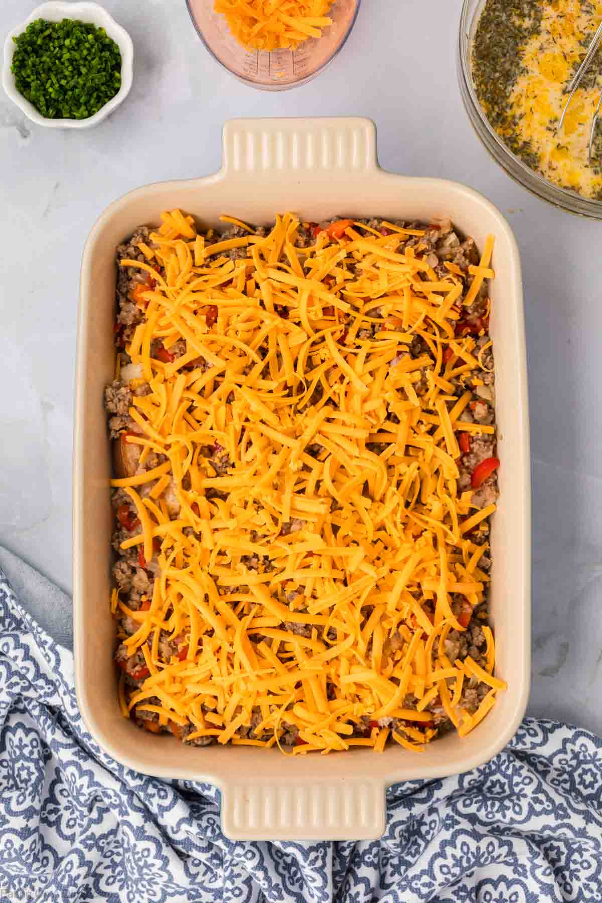 Layering the sausage mixture in the baking dish topped with shredded cheese