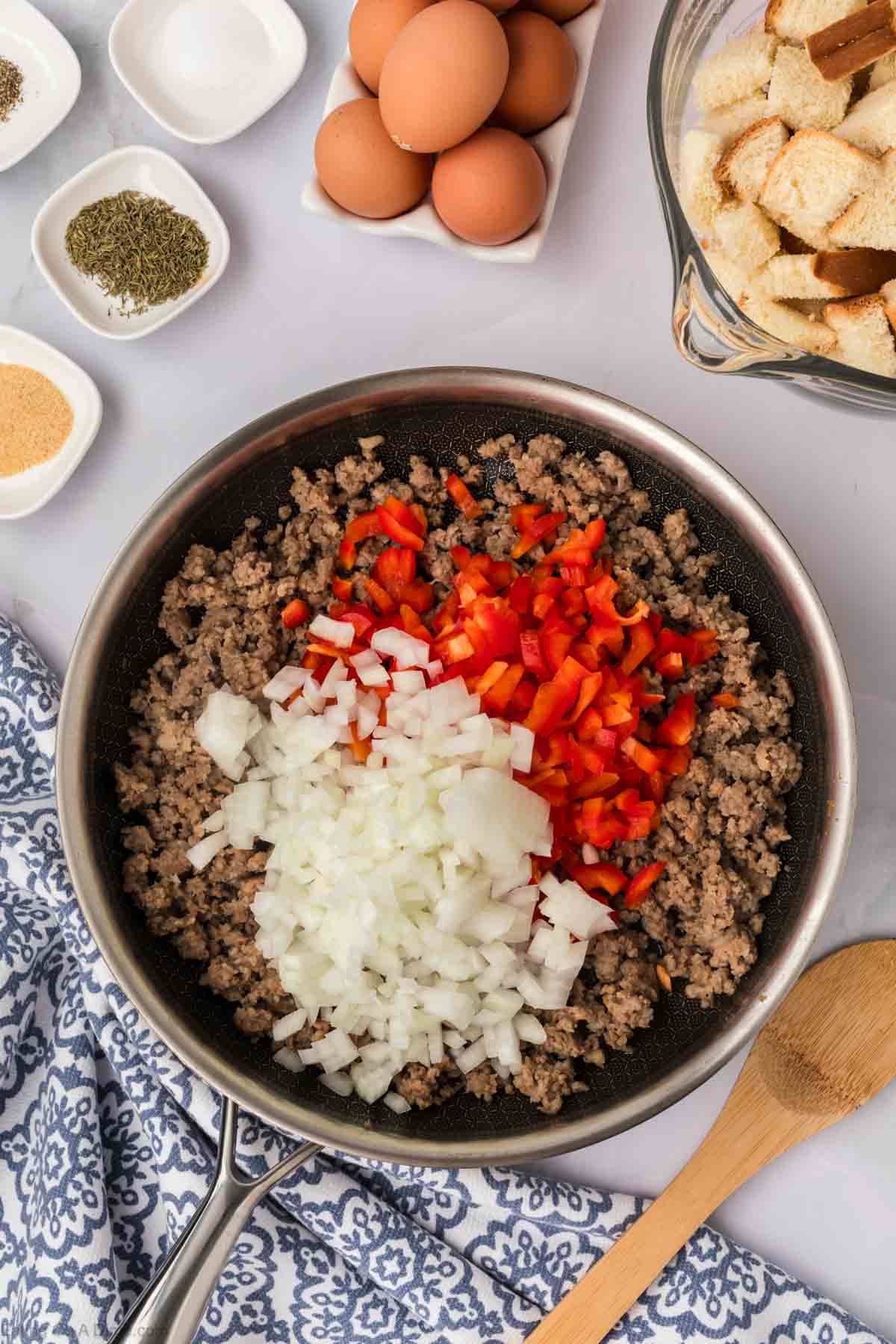 Cooked sausage in a skillet with diced onions and red bell peppers on top