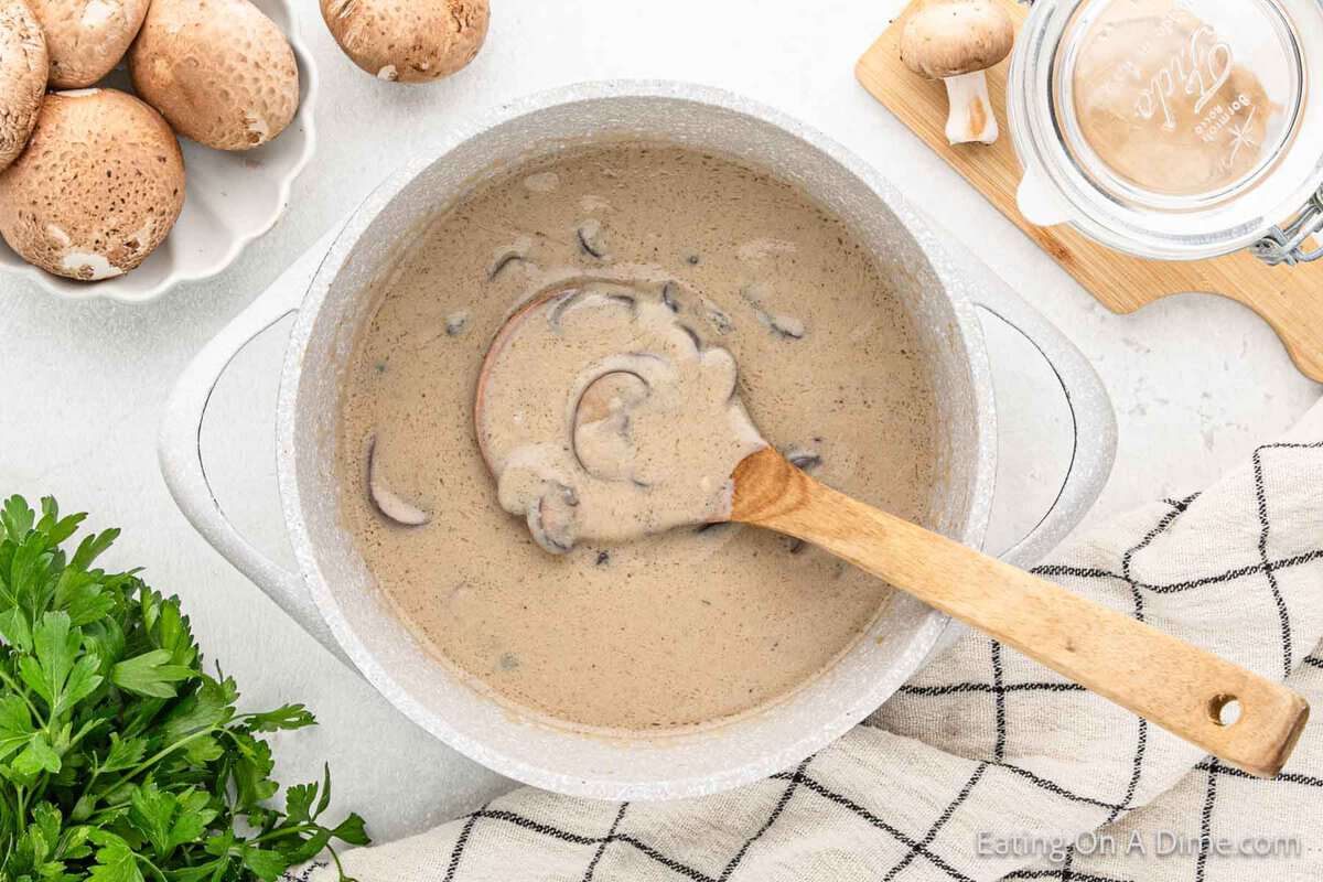 Cream of mushrooms in a large pot with a wooden spoon