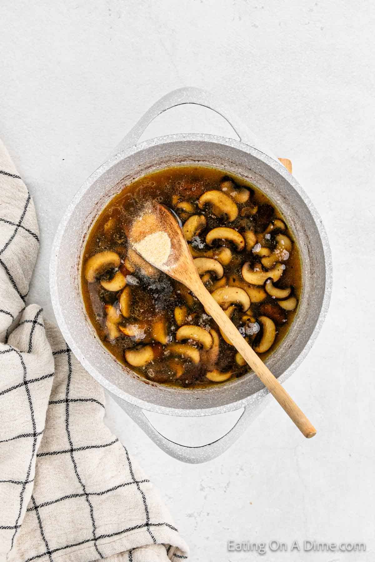 Cooked mushrooms in a large pot with a wooden spoon in broth with spices