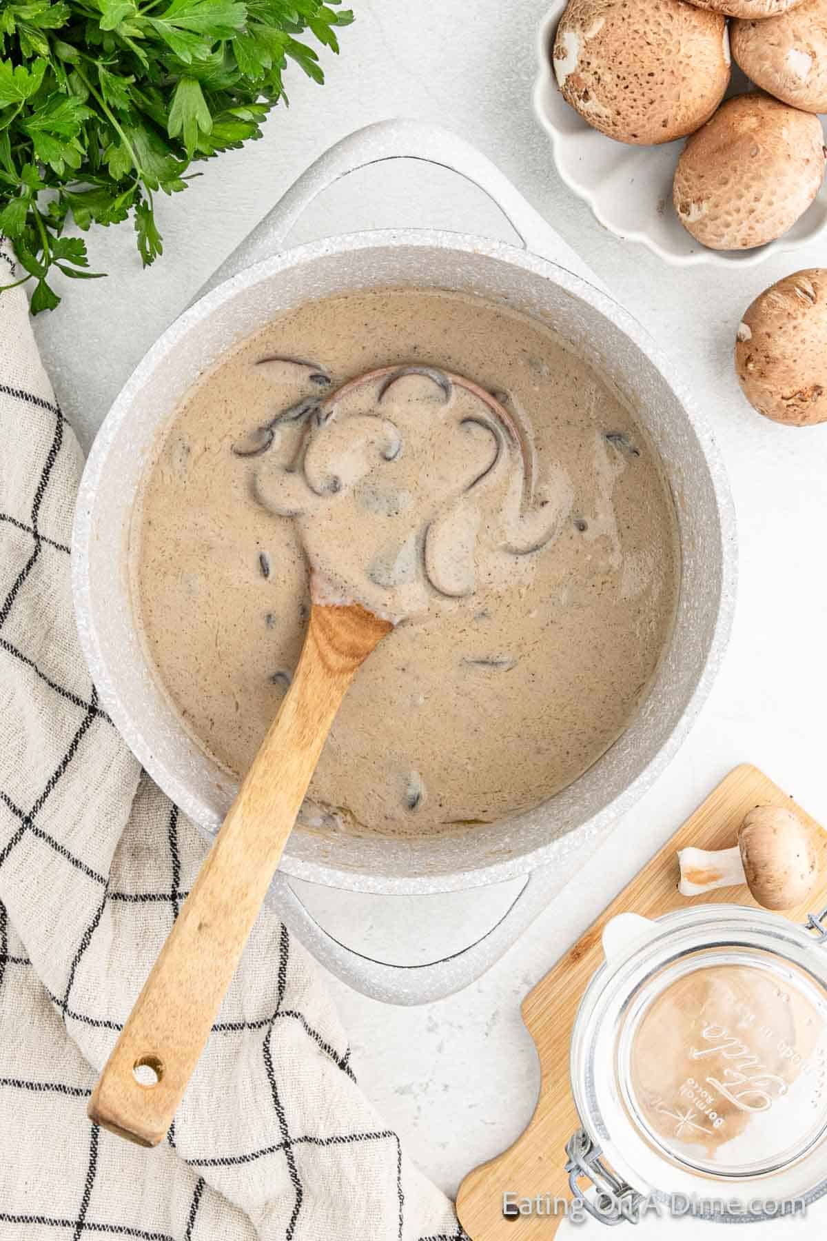 Cream of mushrooms in a large pot with a wooden spoons