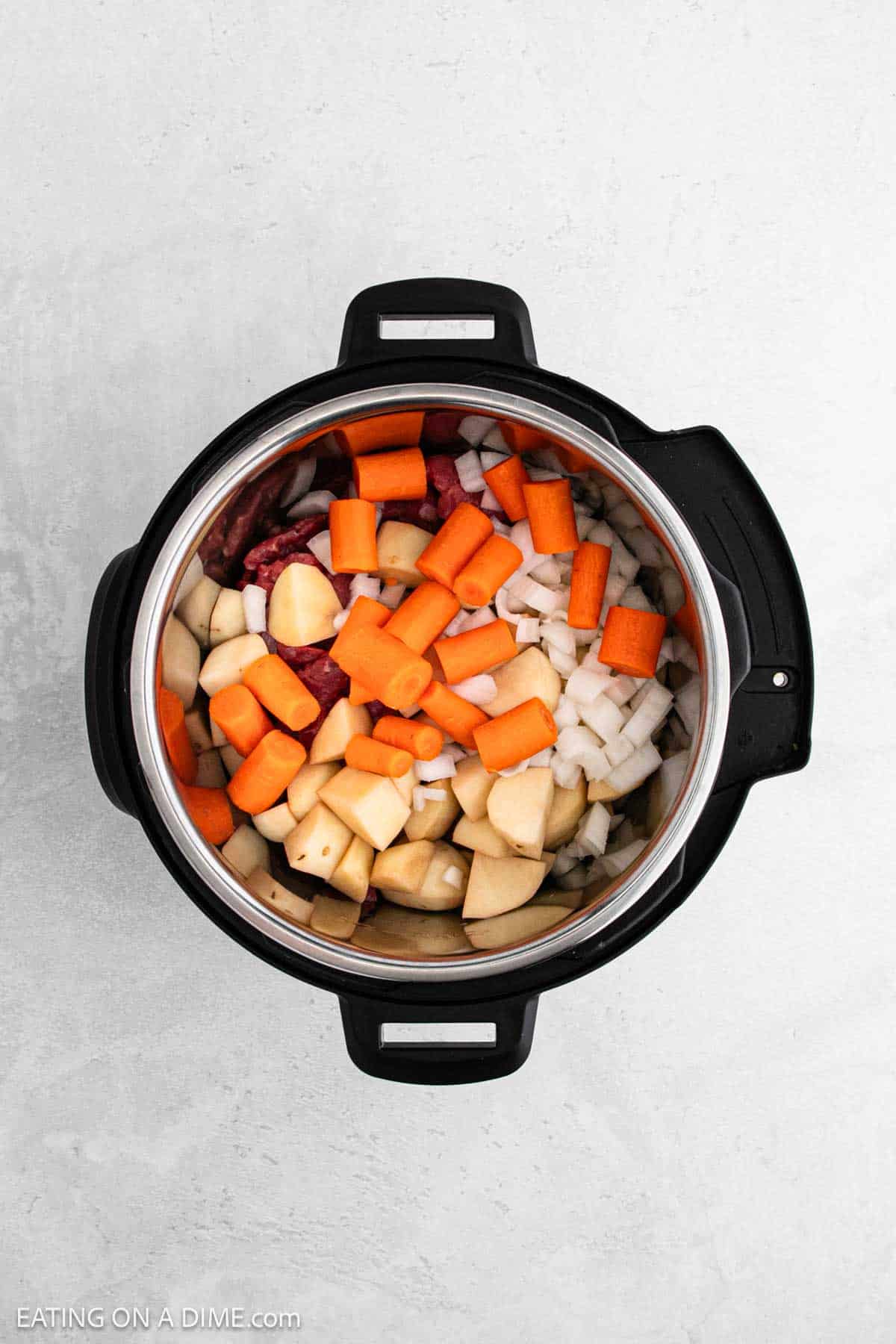 An Instant Pot beef stew recipe featuring chopped carrots, potatoes, onions, and hearty chunks of meat is ready for cooking against a light gray background.