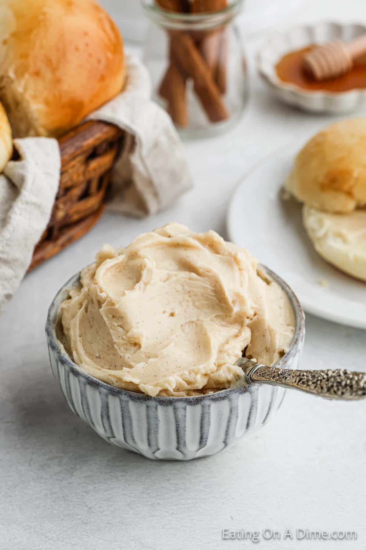 Cinnamon butter in a bowl with a knife with a basket of rolls in the background