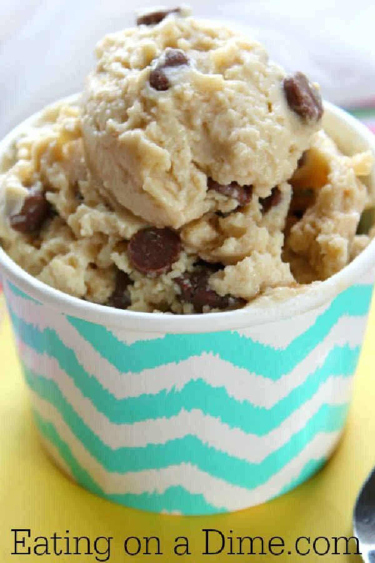 A pastel blue and white zigzag-patterned cup brimming with chocolate chip cookie dough frozen yogurt. The image features text at the bottom that reads "Eating on a Dime.com.