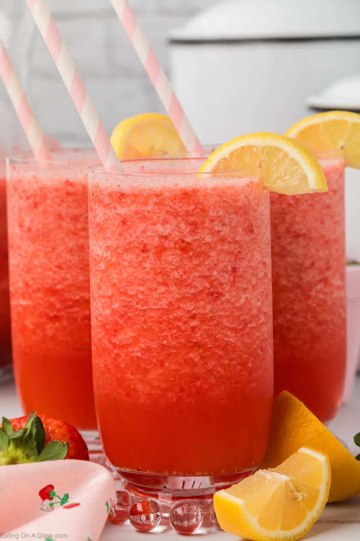 Strawberry Slushie Drink in clear glasses with lemon wedges on the side with pink strip straws inserted into the drink