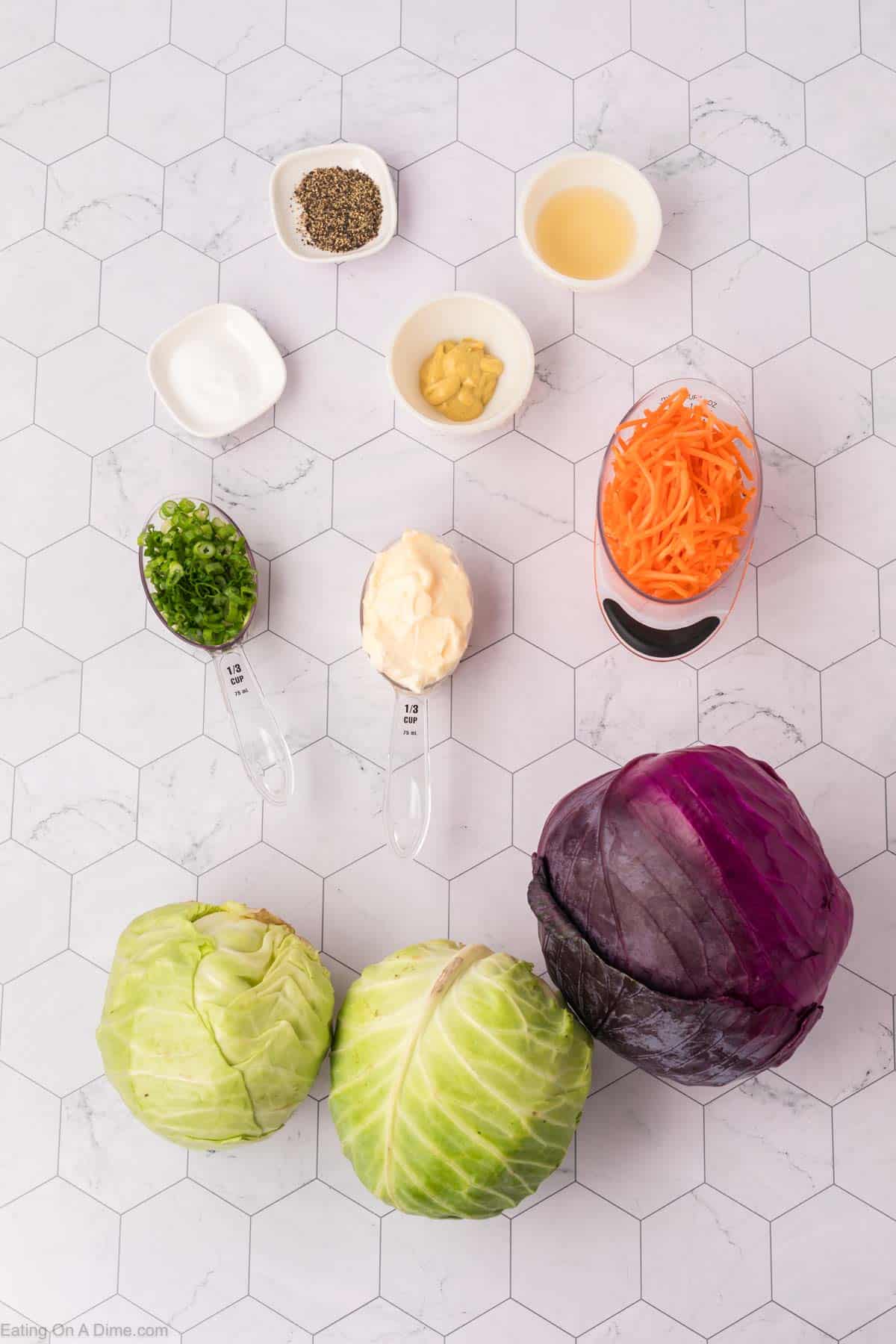 Ingredients for the best coleslaw recipe are artfully arranged on a hexagonal tile surface: shredded carrots, red and green cabbage, mayonnaise, sliced green onions, mustard, sugar, apple cider vinegar, salt, and pepper. Every item is precisely measured in bowls and spoons.