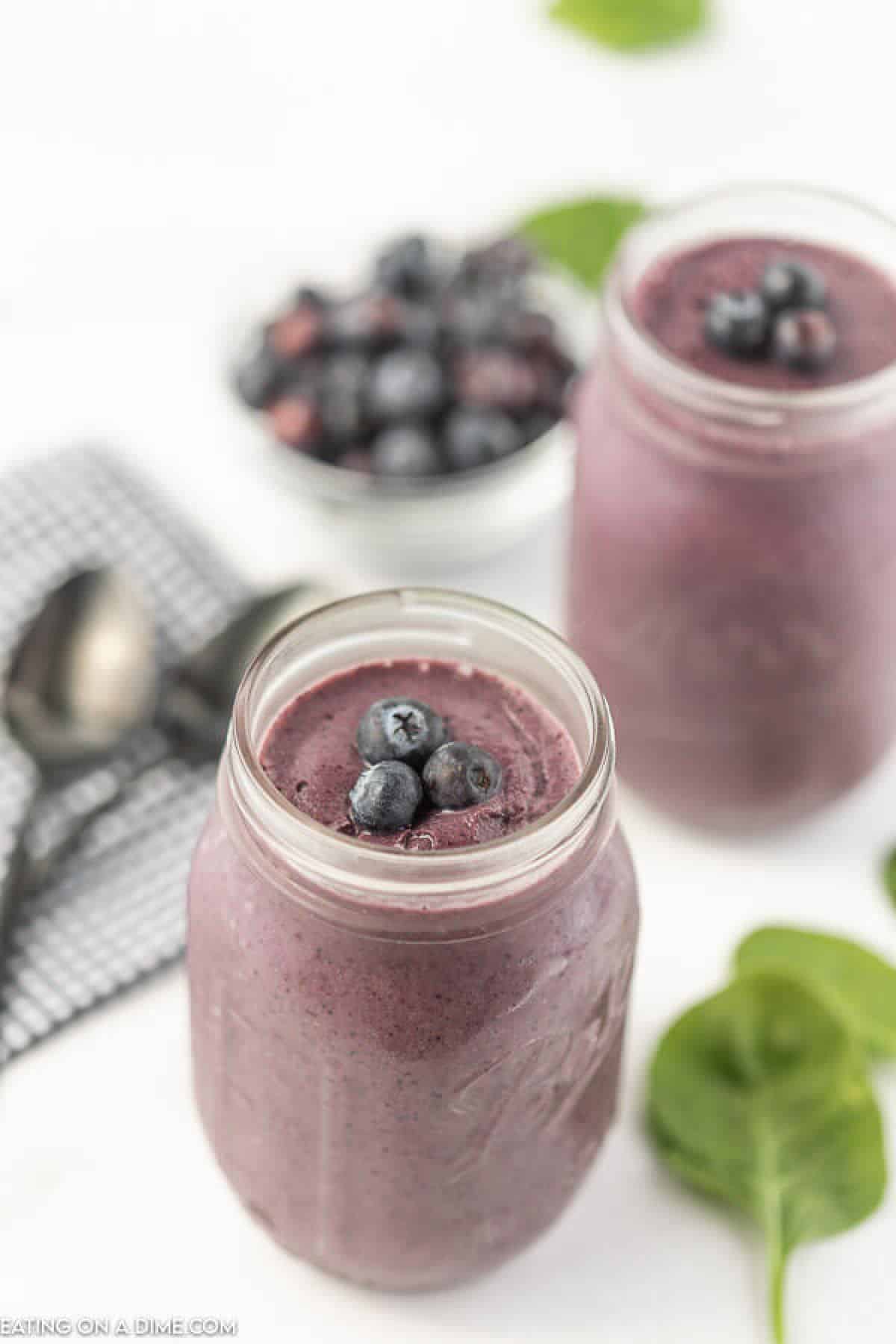 Blueberry Spinach Smoothie with 2 spinach leaves and 2 spoons in the background. 