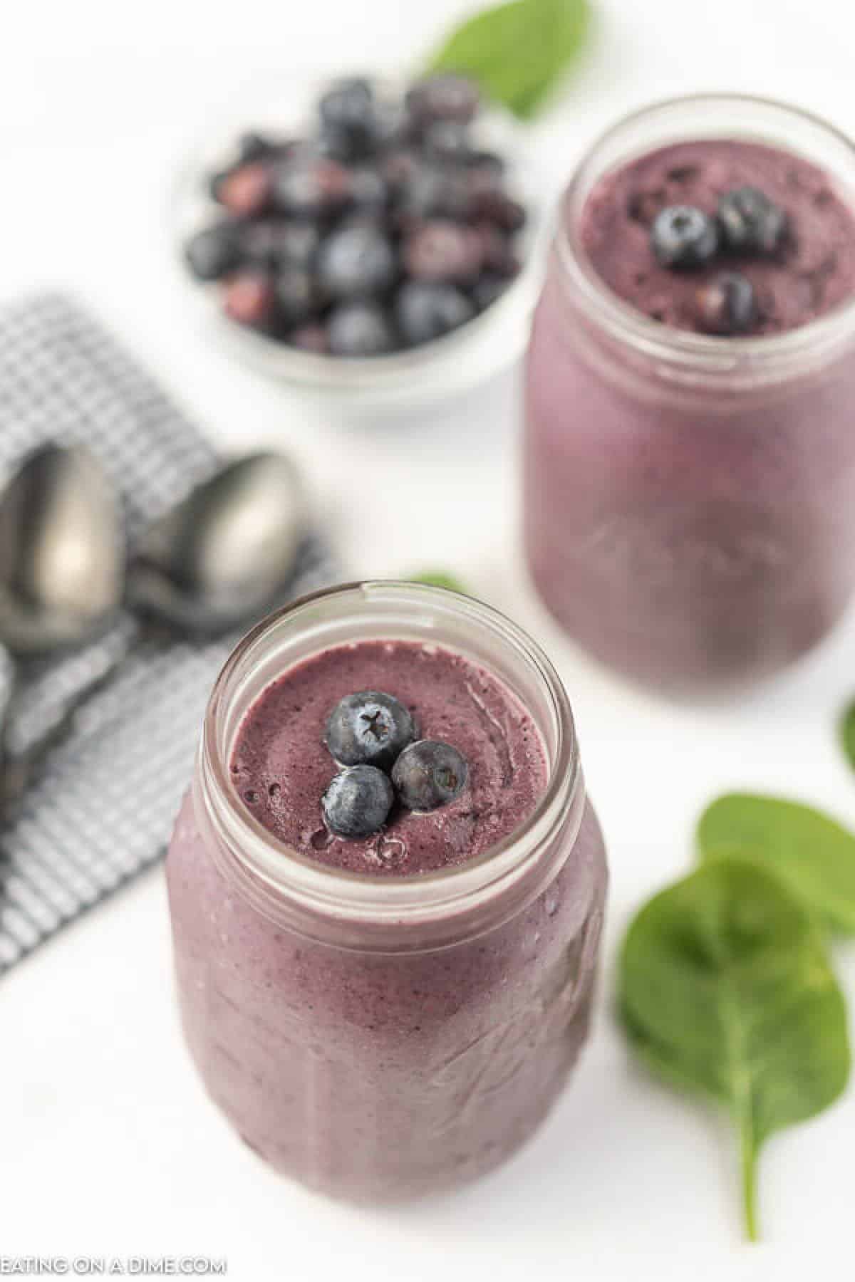 Overview of a Blueberry Spinach Smoothies with another smoothie in the background and a bowl of blueberries in the background too. 