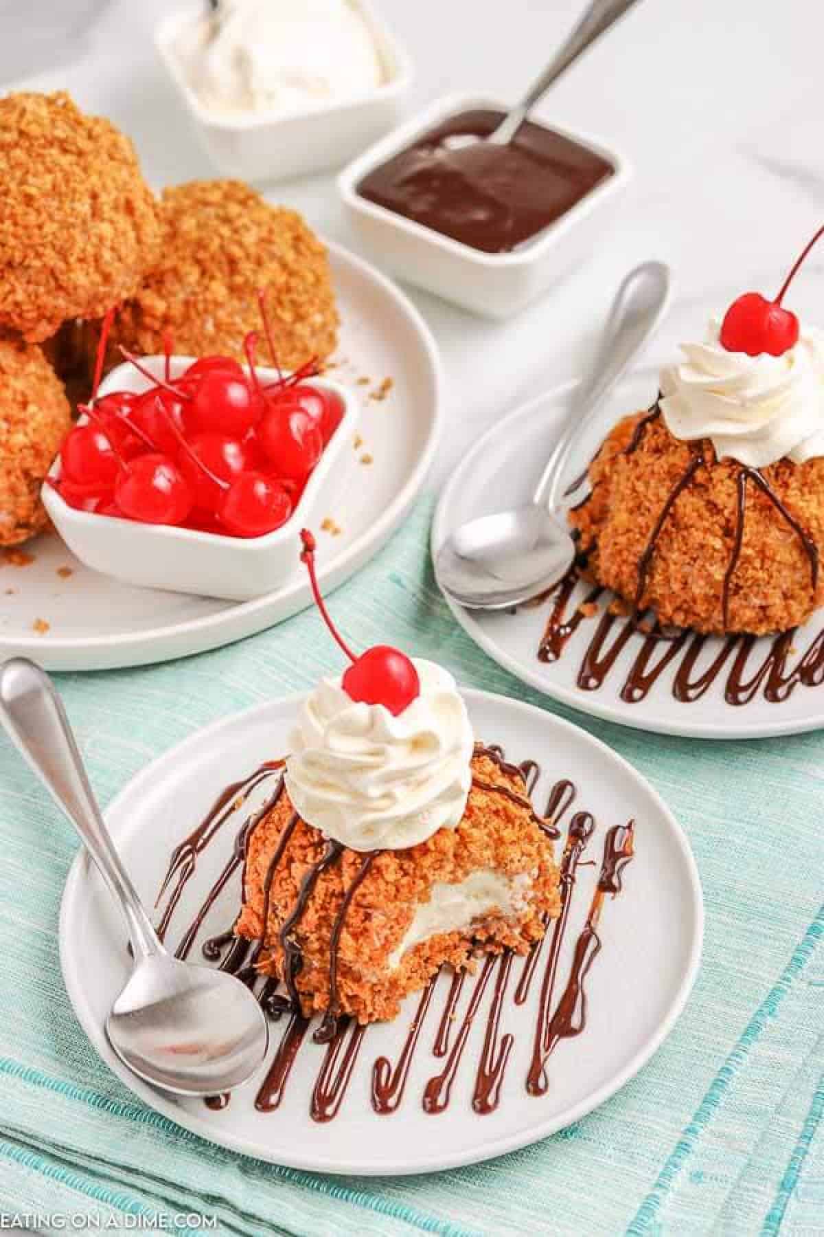 Fried Ice Cream on a white plate topped with whipped cream and a cherry. There is another plate in the back ground with more fried ice cream topped with whipped cream and a cherry. 