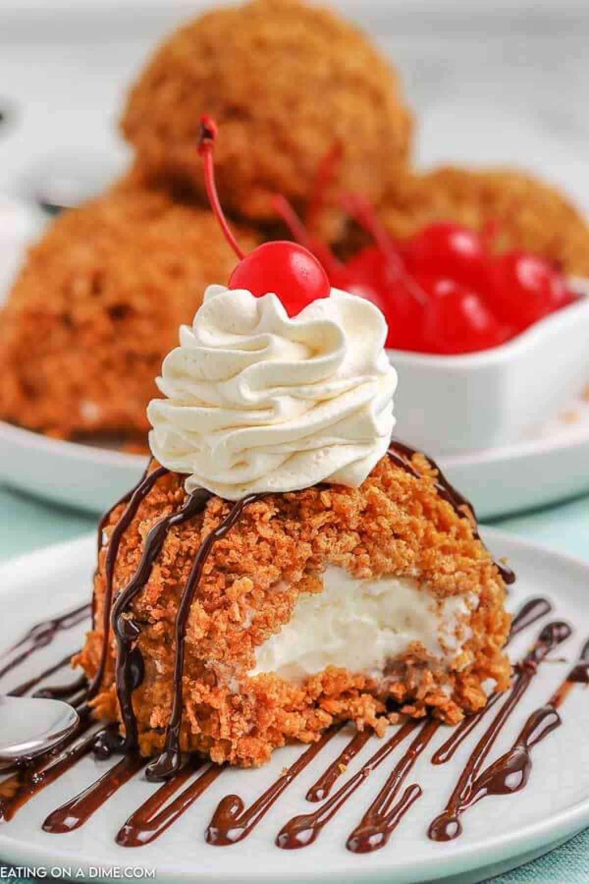 Fried Ice Cream on a white plate topped with whipped cream and a cherry. There is another plate in the back ground with more fried ice cream topped with whipped cream and a cherry. 