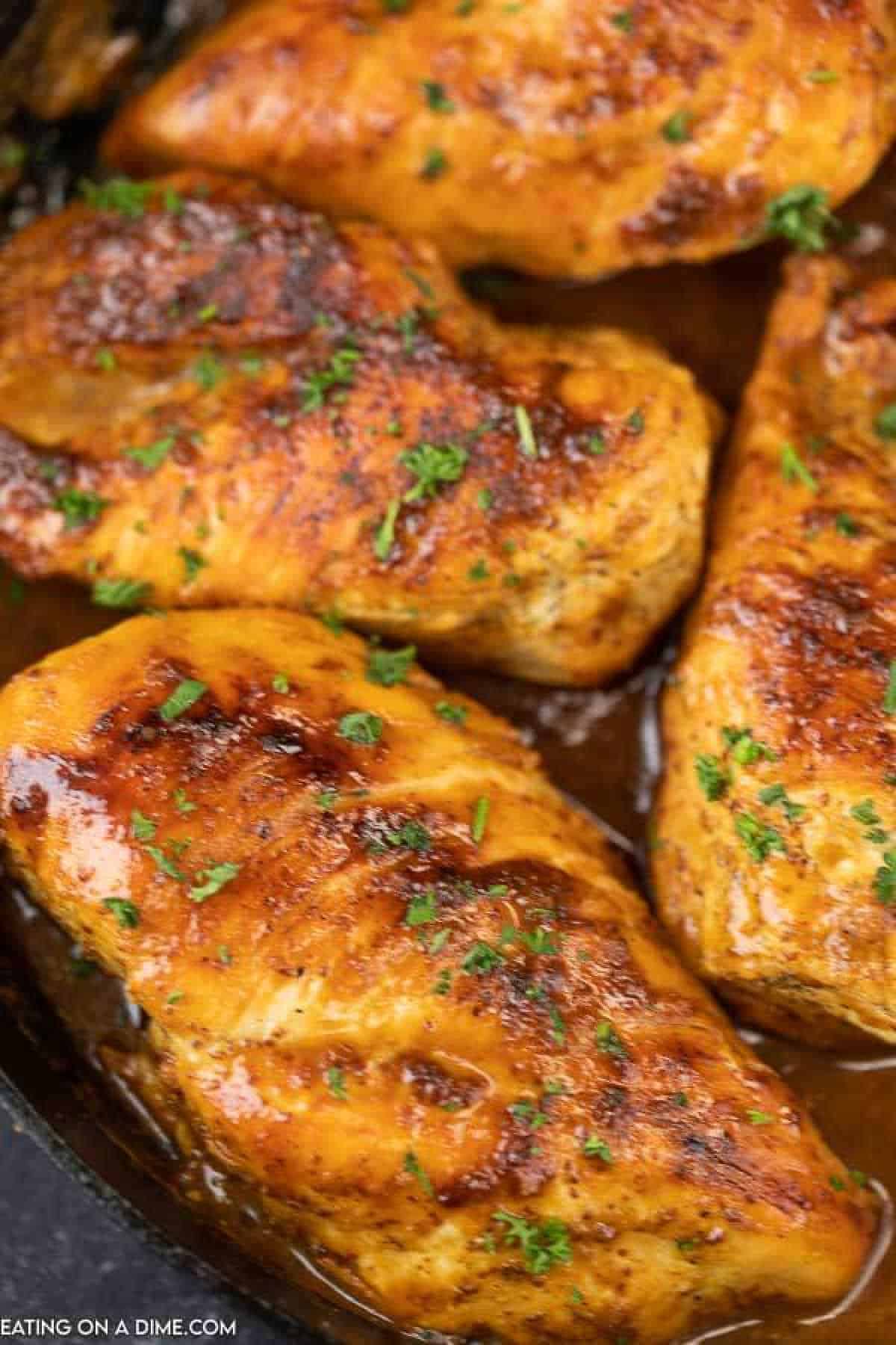 Close-up of grilled honey mustard chicken breasts seasoned with herbs, glistening with sauce, and garnished with chopped parsley in a skillet. The chicken appears juicy and well-cooked, showcasing a golden-brown color.