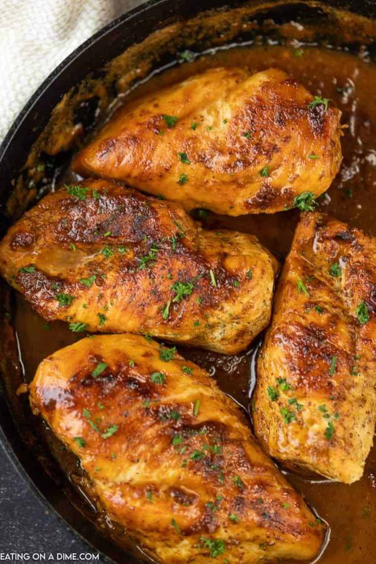 Four seasoned and grilled chicken breasts sizzle in a skillet, garnished with chopped parsley. Coated in a golden-brown honey mustard glaze sprinkled with spices, they rest in a rich, brown sauce perfect for this delectable chicken recipe.