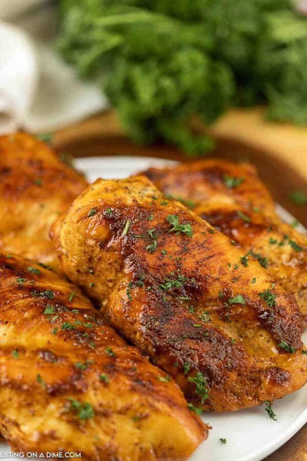 Grilled honey mustard chicken breasts seasoned with herbs and spices on a white platter. Parsley is sprinkled on top, and fresh parsley is in the background, completing this delightful recipe.