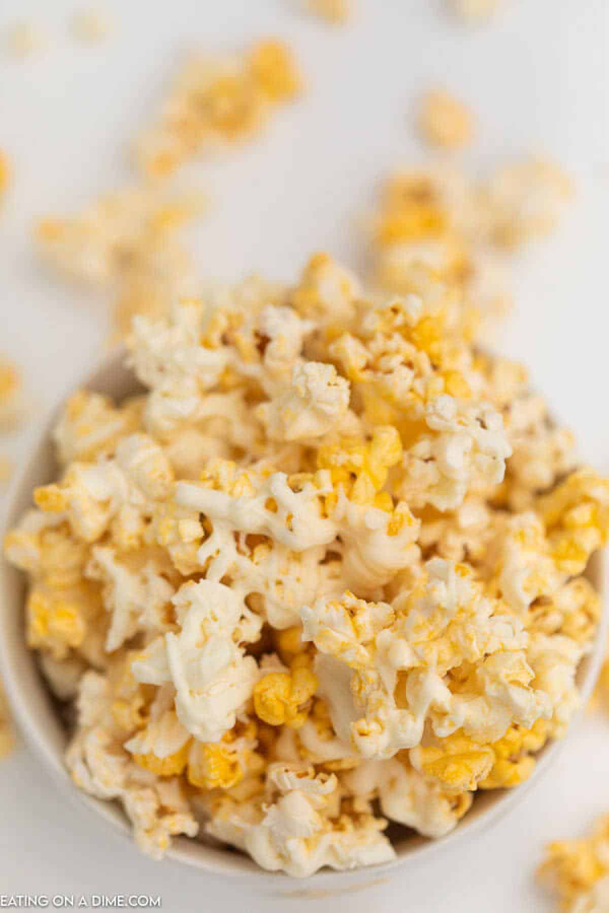 A close-up of a bowl filled with freshly popped popcorn, featuring a delicious mix of buttery yellow and white kernels. Some pieces, perfect for a white chocolate popcorn recipe, are scattered around the bowl on a pristine white surface.