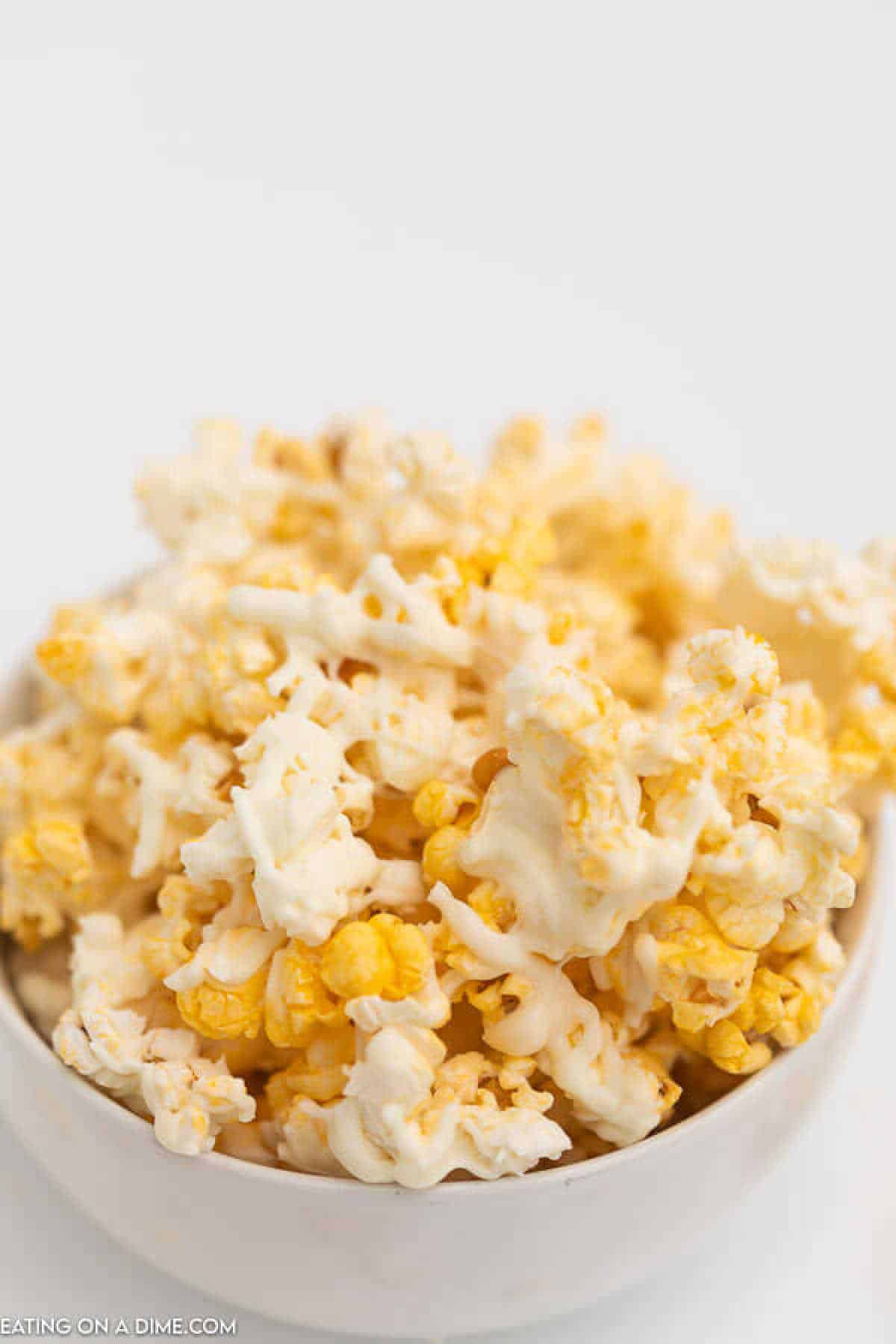 A bowl of popcorn drizzled with a rich, white chocolate topping mixed with vibrant yellow accents.