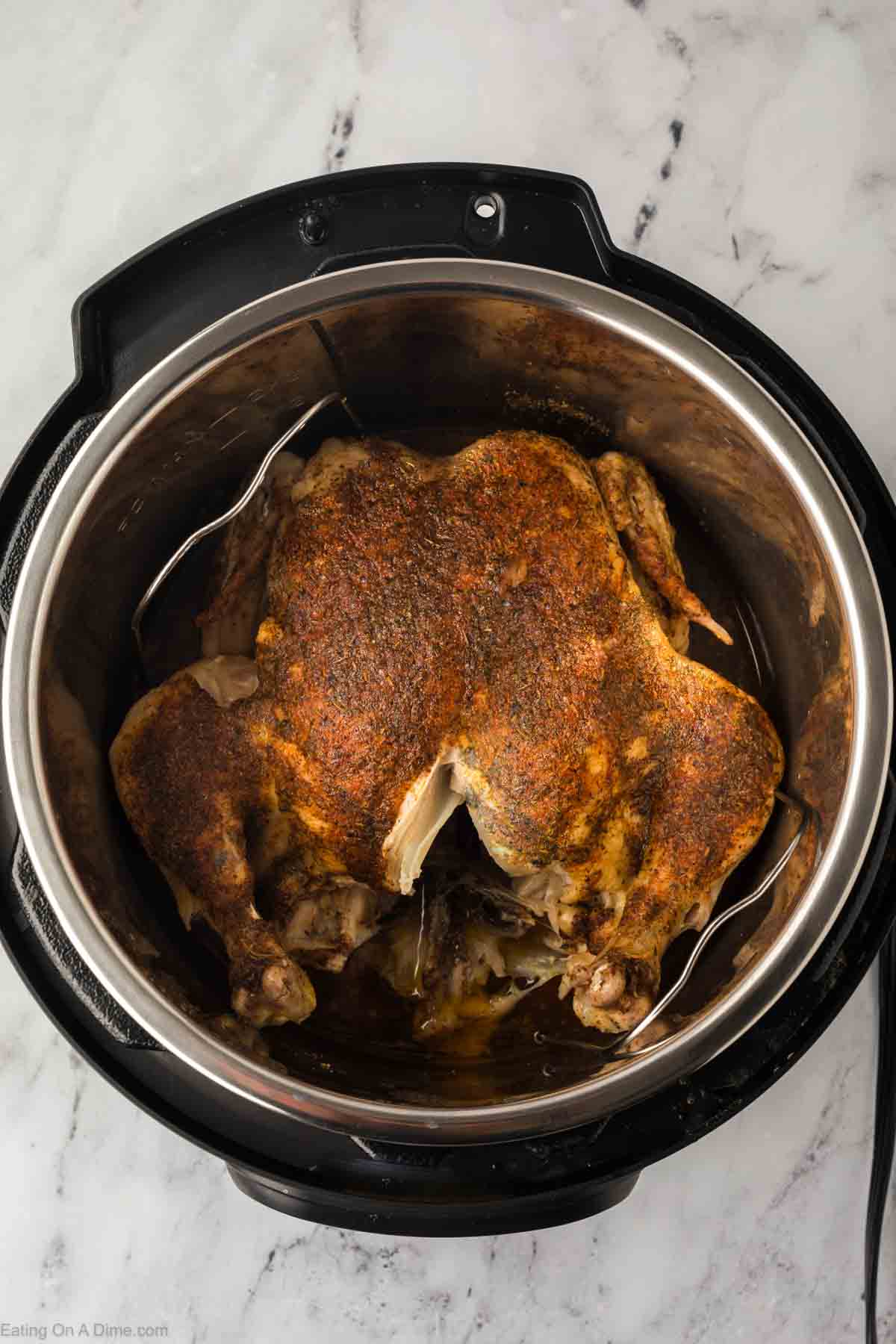 An overhead view reveals a succulent Instant Pot Whole Chicken, perfectly seasoned and cooked to golden-brown perfection on a marble countertop. The gleaming skin is irresistibly inviting, and a flavorful liquid pools at the bottom of the pot, promising delicious depth.