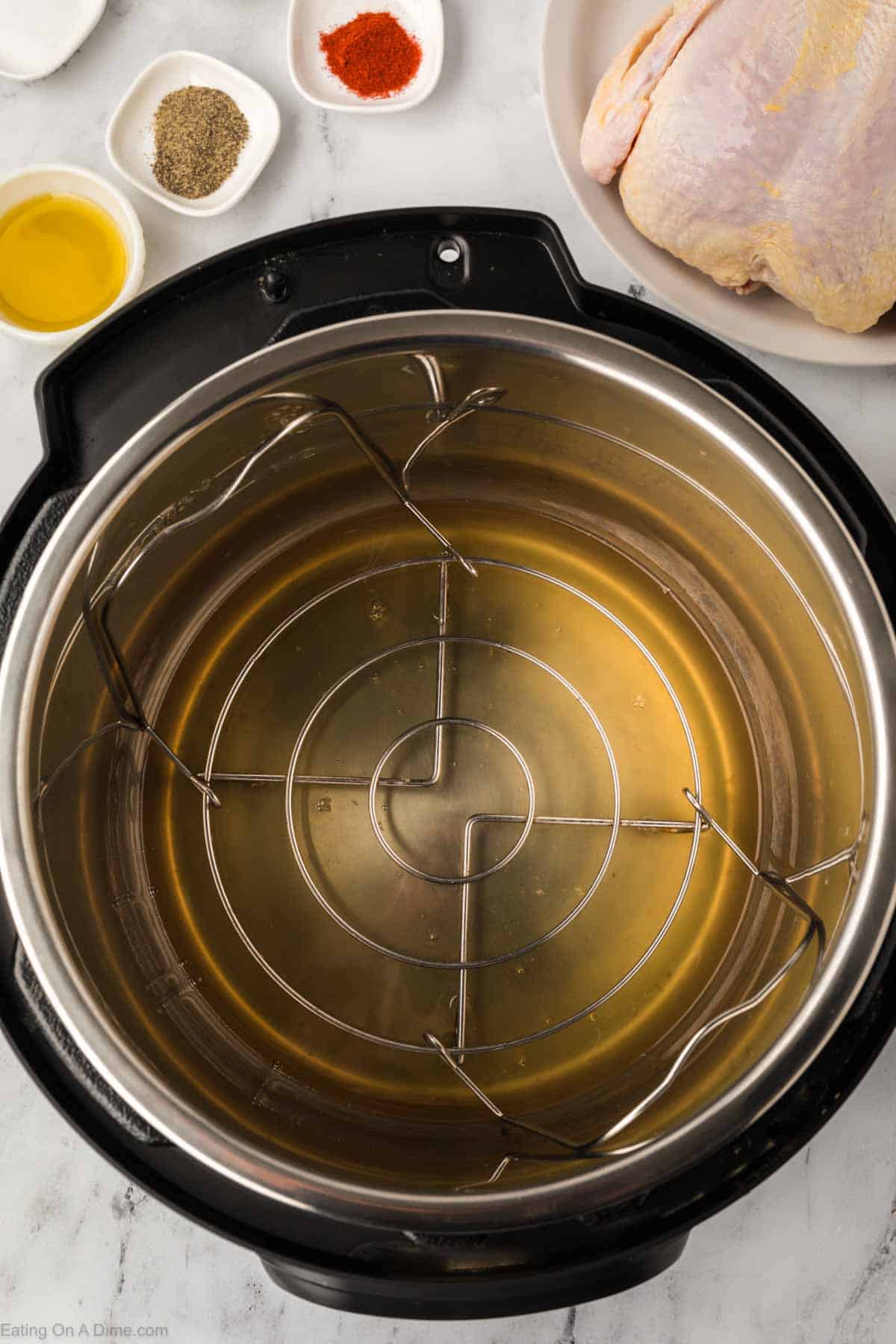 An Instant Pot Whole Chicken setup graces the marble countertop, complete with liquid inside and surrounded by chicken, olive oil, and small bowls of seasonings.