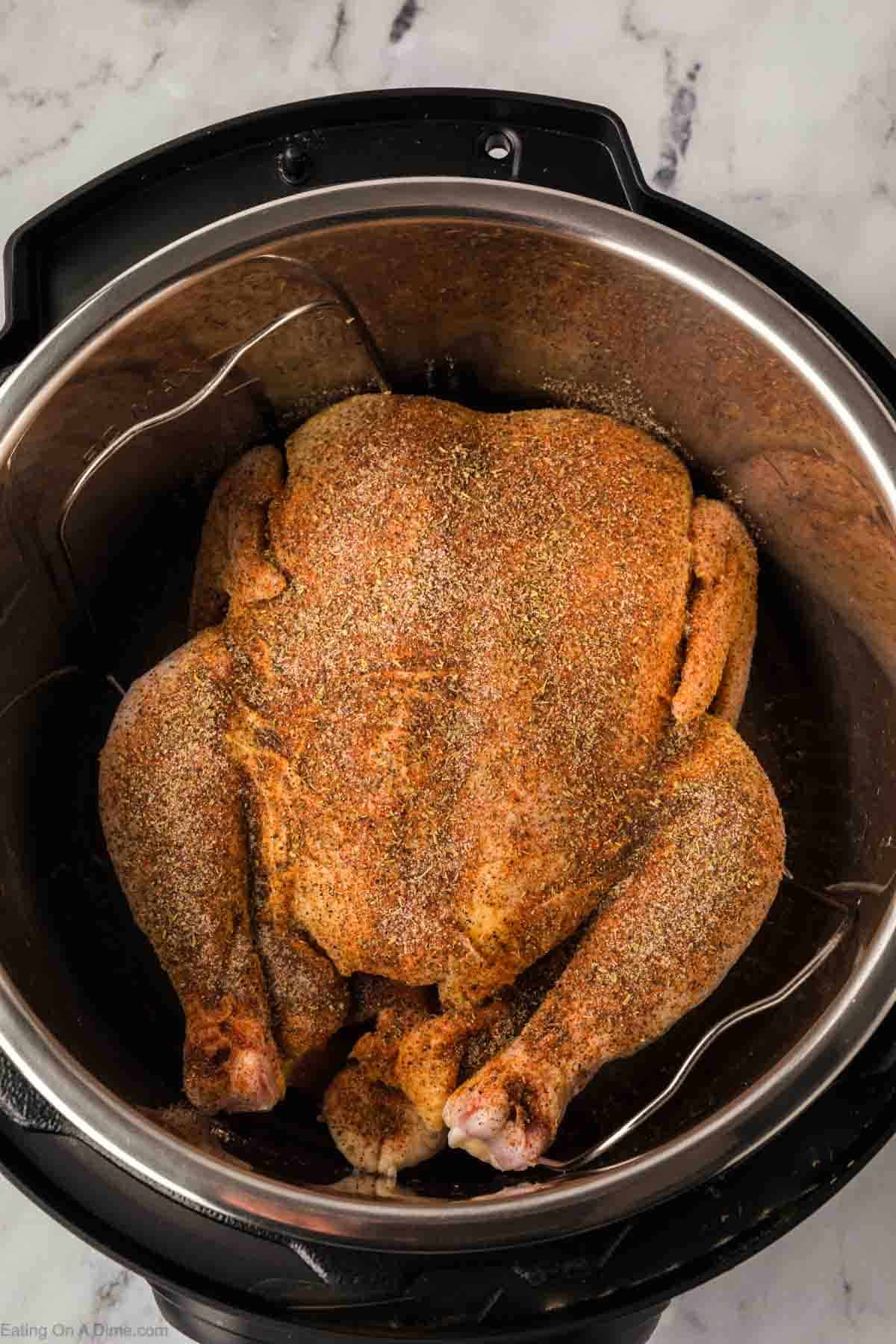 A whole chicken, seasoned with herbs and spices, sits inside an Instant Pot on a marble surface, ready to transform into a delicious meal. The close-up reveals the flavorful coating that makes this Instant Pot whole chicken irresistibly aromatic before cooking even begins.