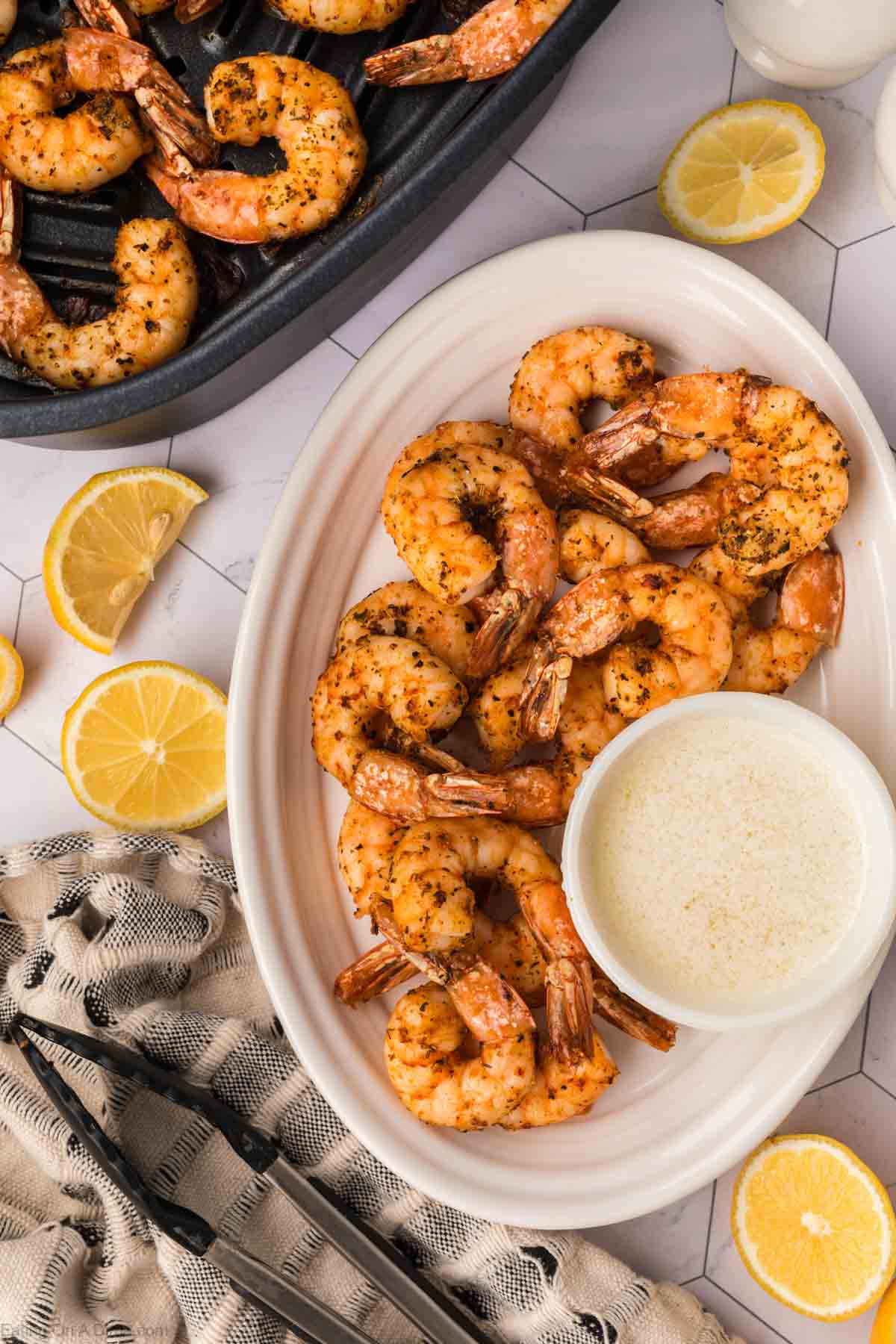 Air Fryer Shrimp stacked on a plate with a side of melted butter and shrimp in a air fryer basket