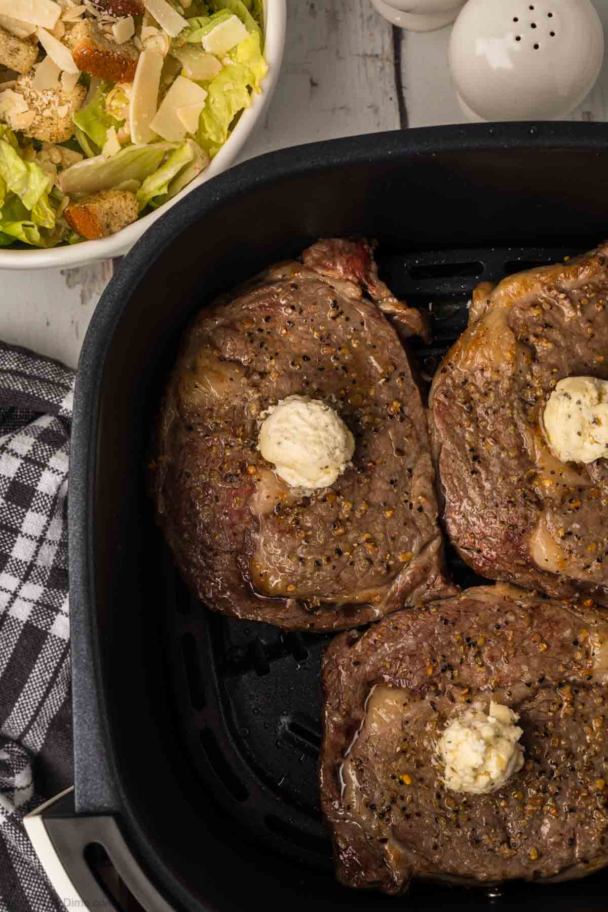 Cooked steak in air fryer basket topped with melted butter