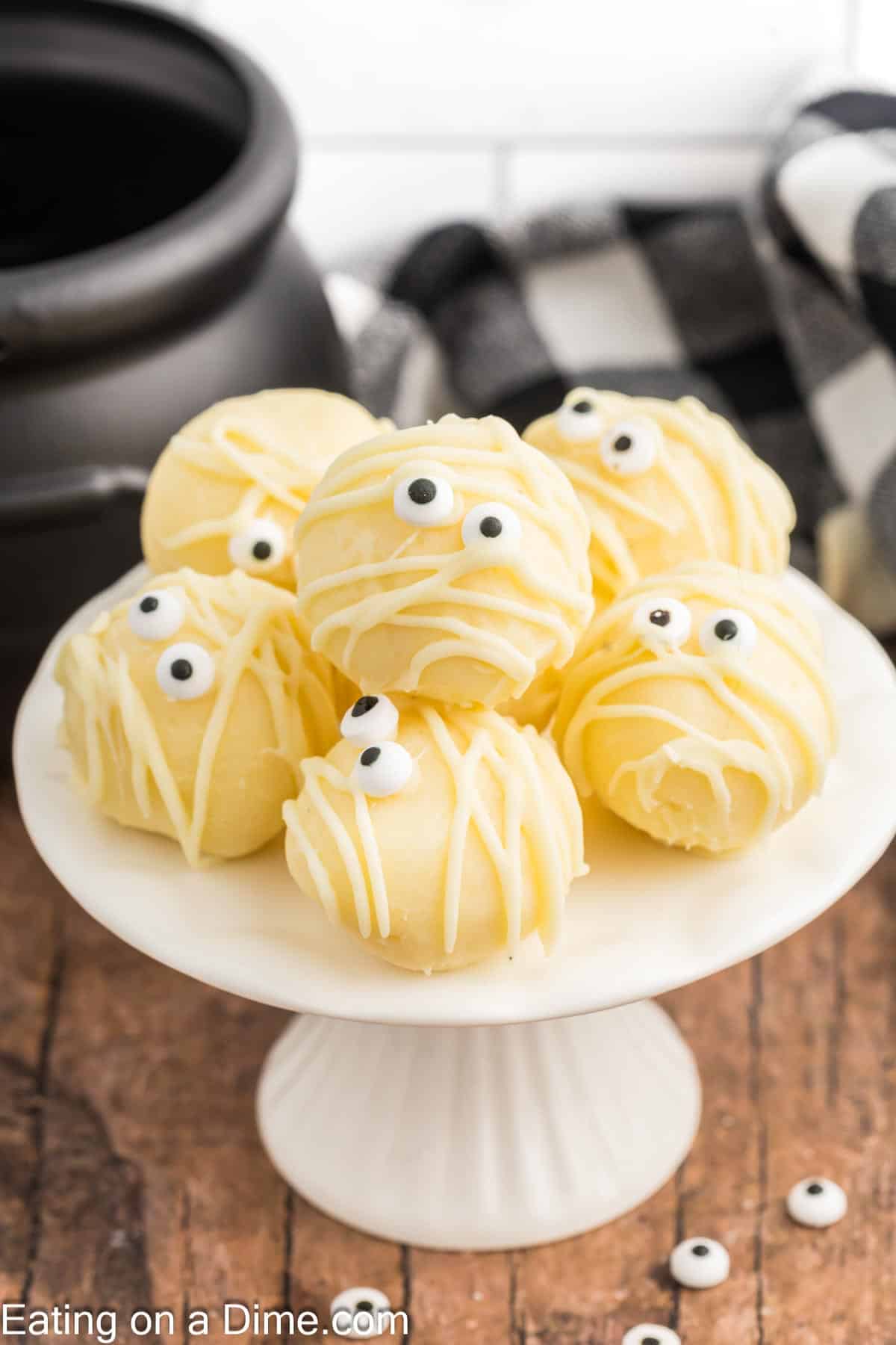 White Chocolate Mummy Truffles decorated with candy eyes and drizzled chocolate on a cake stand