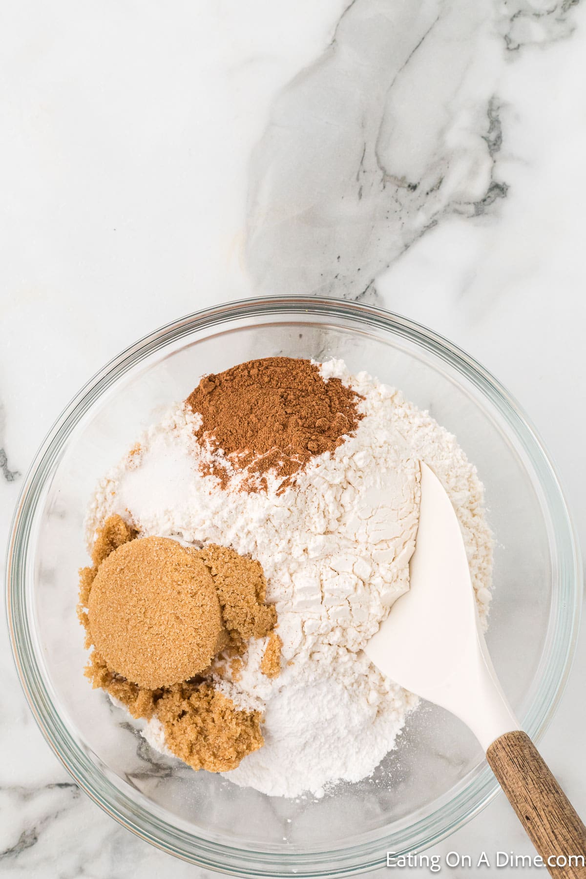 Combining flour, brown sugar, pumpkin spice, salt, and baking powder in a bowl with a spoon