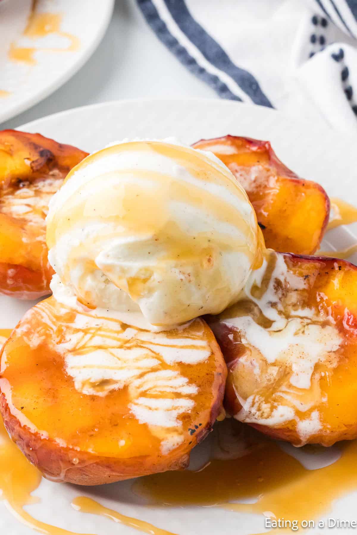 Grilled peach halves on a plate topped with a scoop of vanilla ice cream