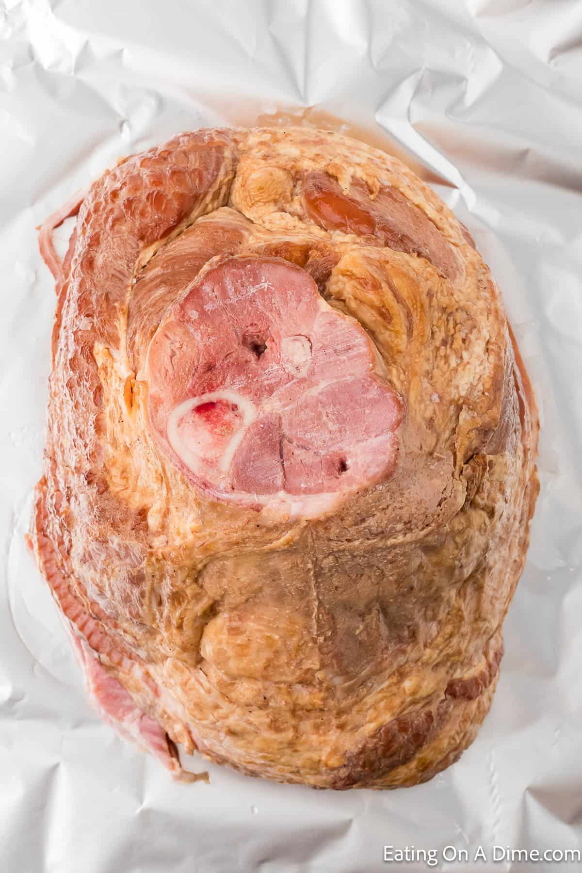 A cooked ham with a visible bone in the center, resting on a sheet of aluminum foil. The ham, prepared using an Instant Pot Spiral Ham Recipe, boasts a glazed, slightly browned surface.