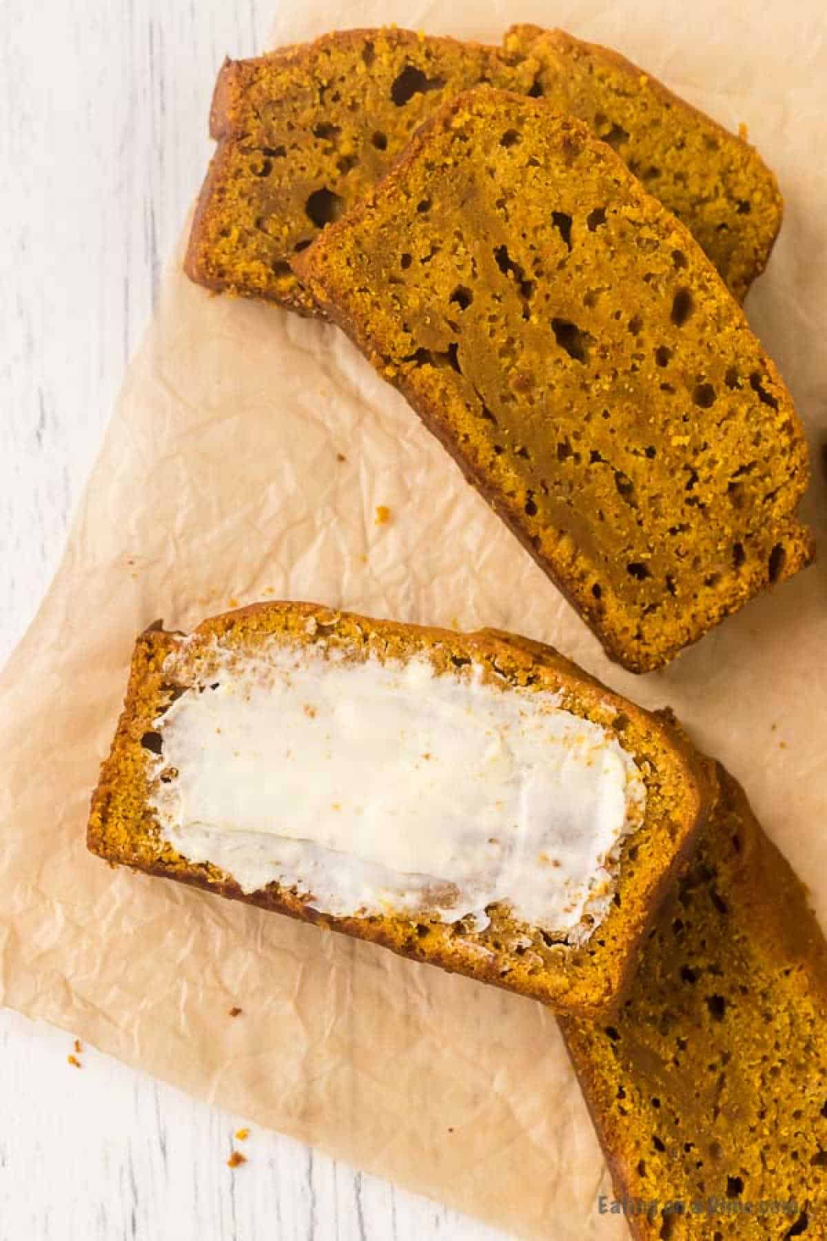 Slices of pumpkin bread, crafted from a beloved recipe, rest on parchment paper with one slice generously spread with butter.