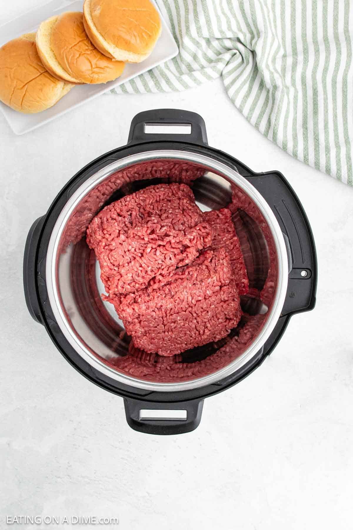 Ground beef for Instant Pot sloppy joes sits ready alongside a plate of hamburger buns. A striped cloth adds a touch of charm, resting against the light gray background.