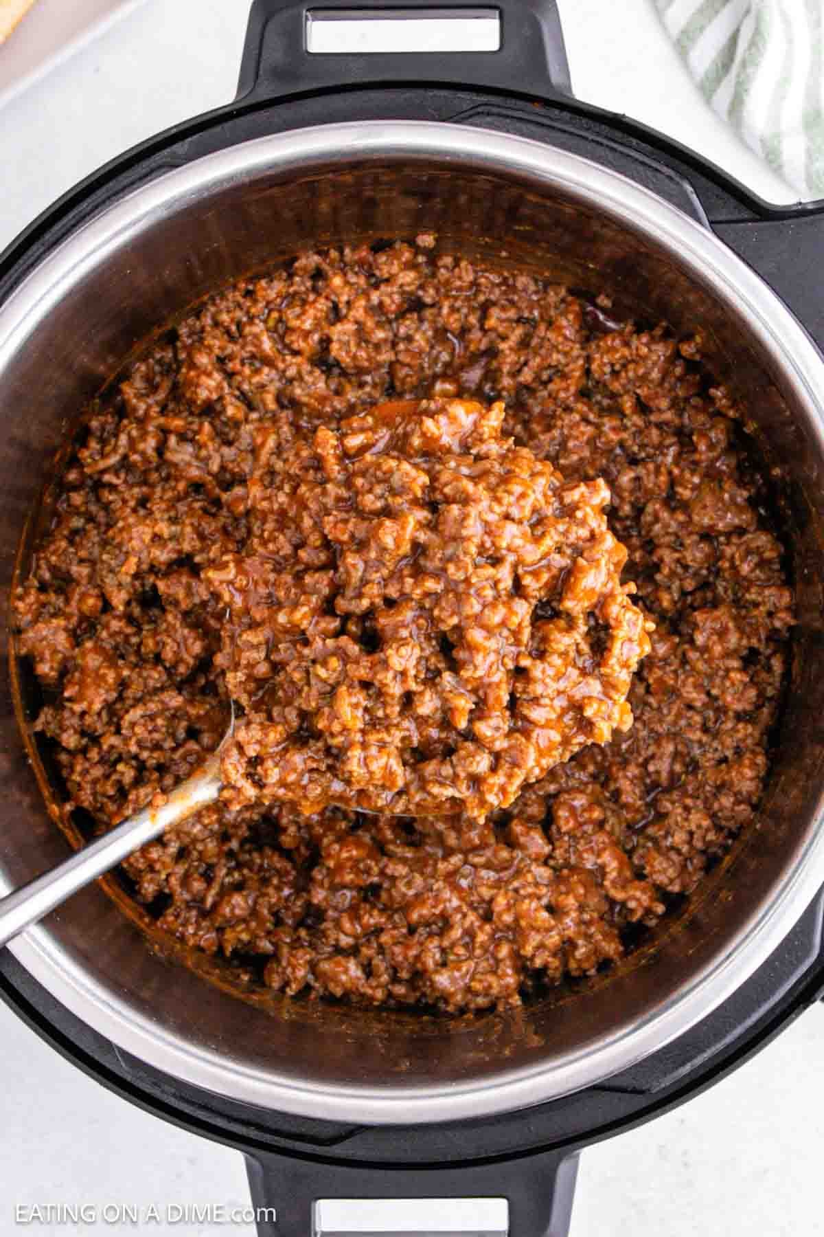 An Instant Pot filled with seasoned ground beef, perfect for sloppy joes. A ladle scoops the rich, saucy mixture, its mouthwatering aroma filling the air. The pot rests on a white countertop with a striped cloth nearby.