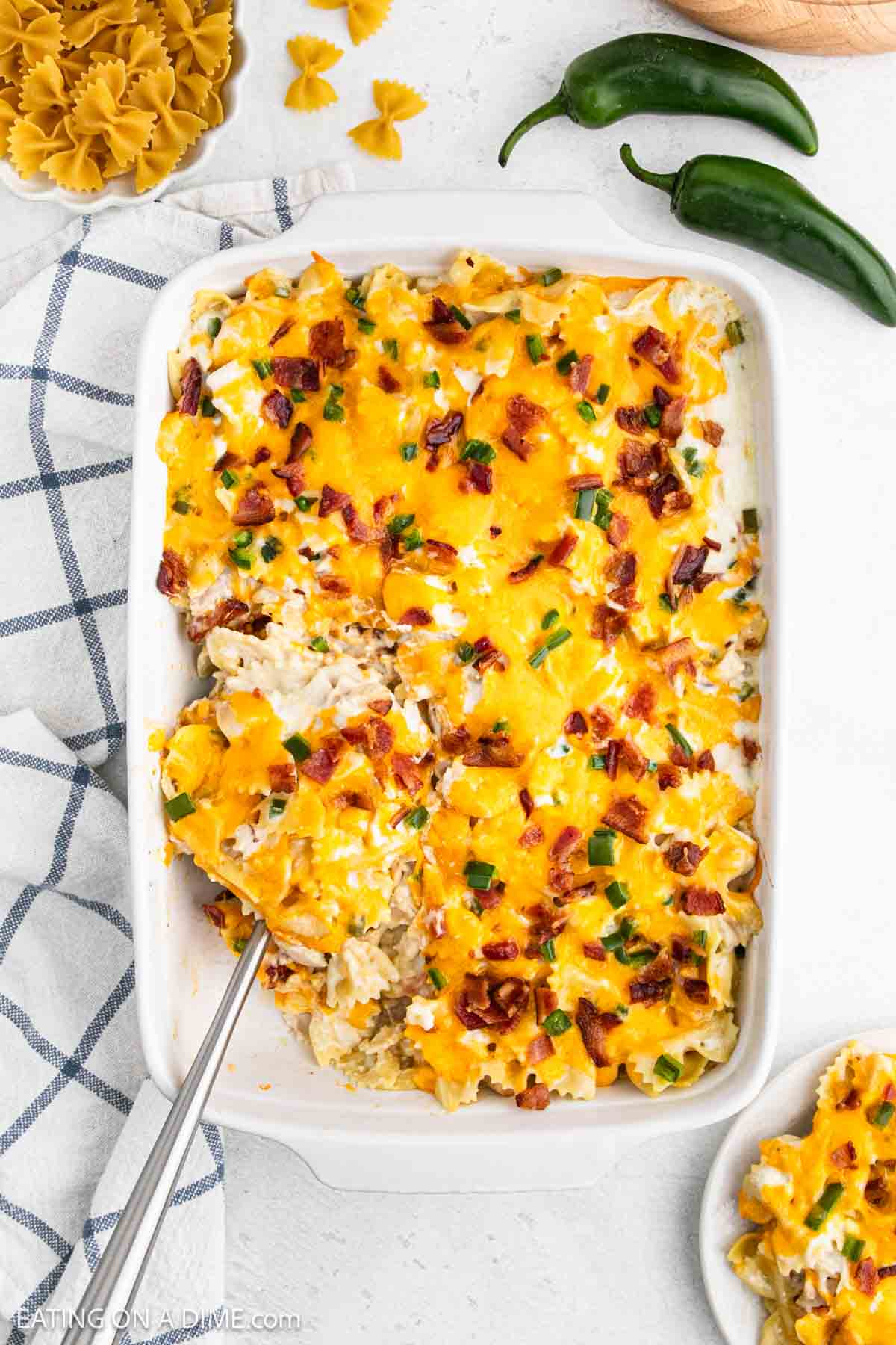 Jalapeno Popper Chicken Casserole topped with melted cheese, chopped bacon and chopped jalapenos in a casserole dish