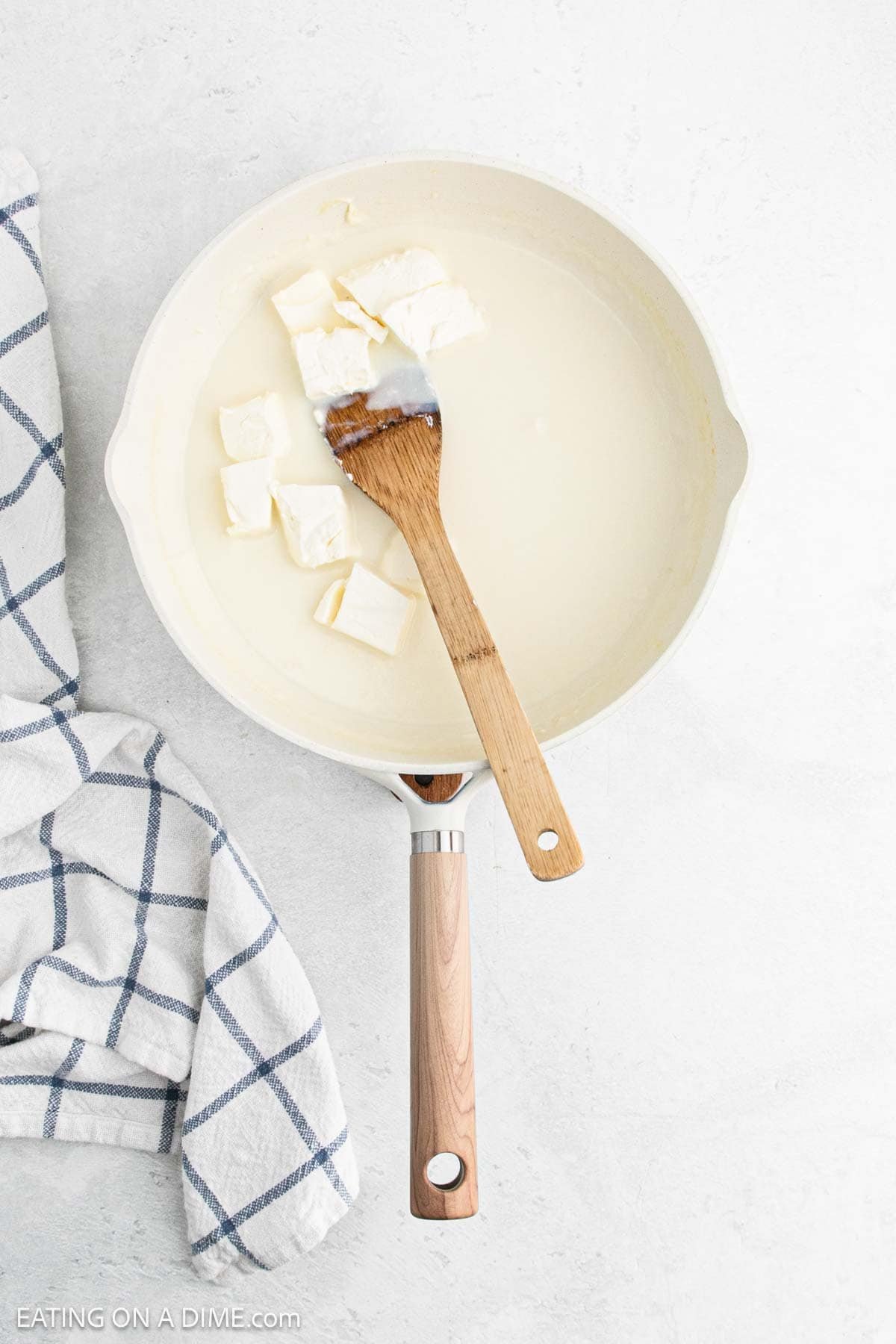 Diced cream cheese mixed into the milk mixture in a skillet with a wooden spoon