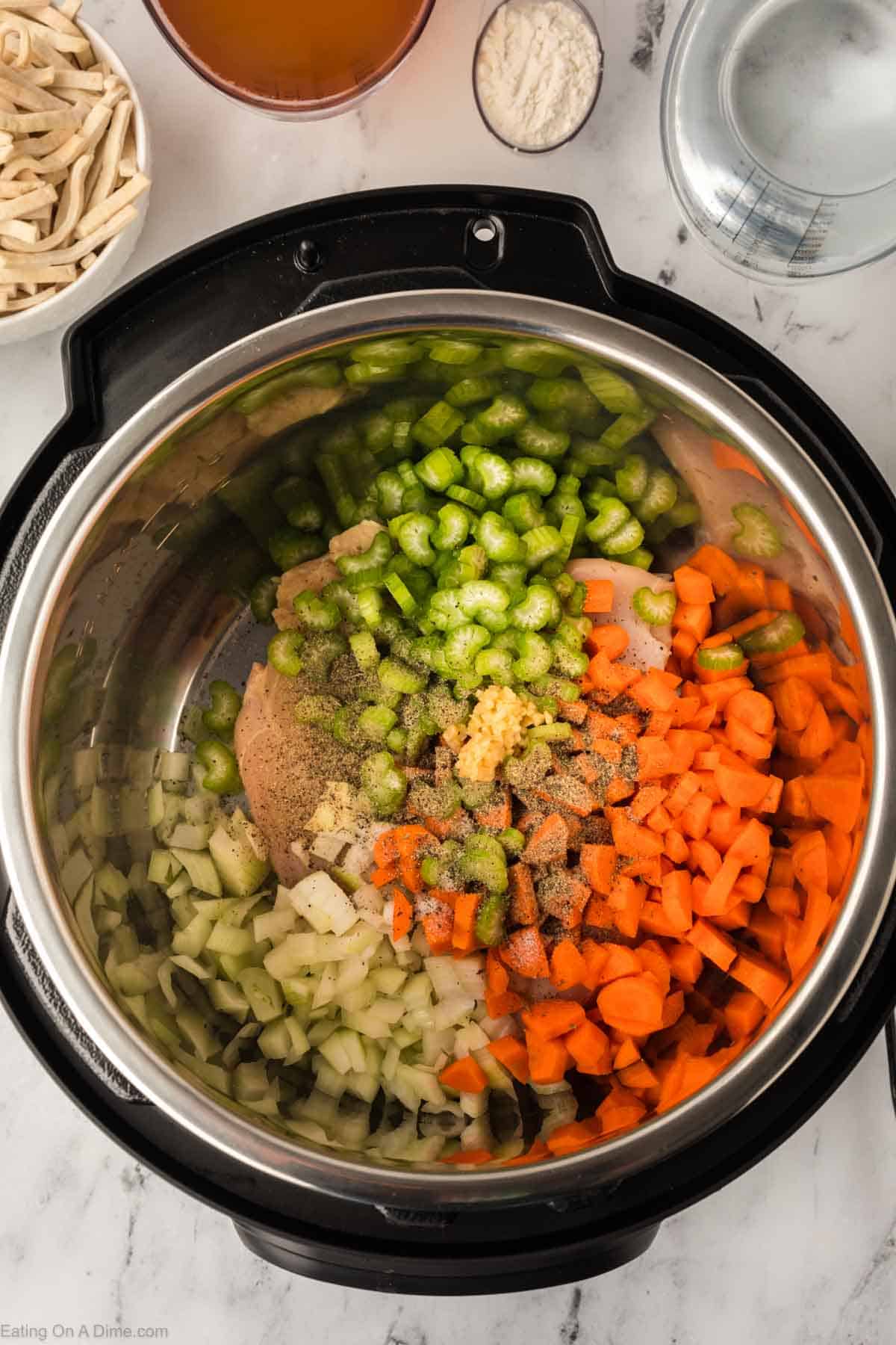 chopped celery, onions, and carrots with chicken breast in the instant pot topped with seasoning and minced garlic